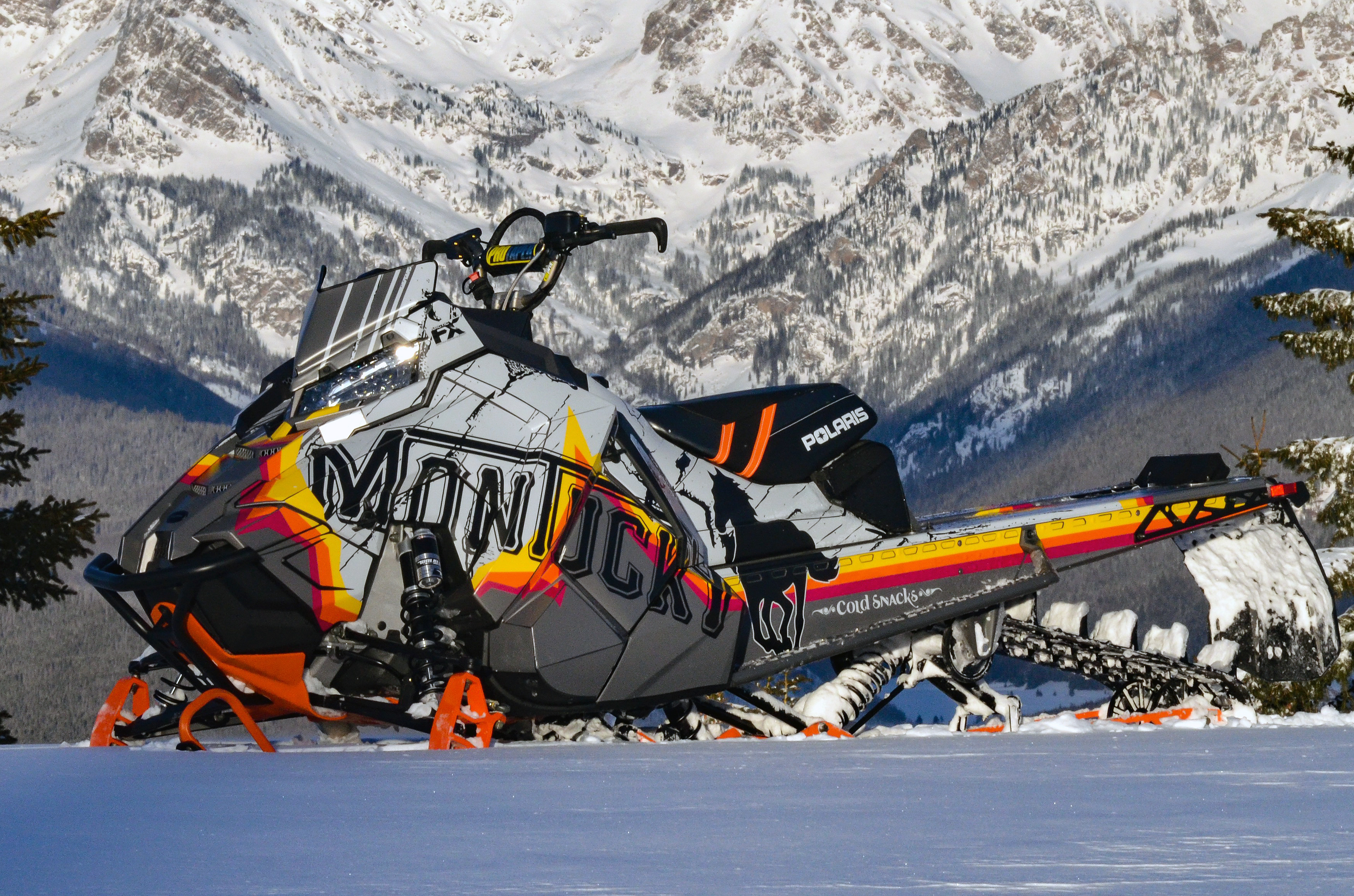 A Polaris Axys Mountain snowmobile with a red, black, orange, and white Montucky Cold Snacks beer custom vinyl wrap.