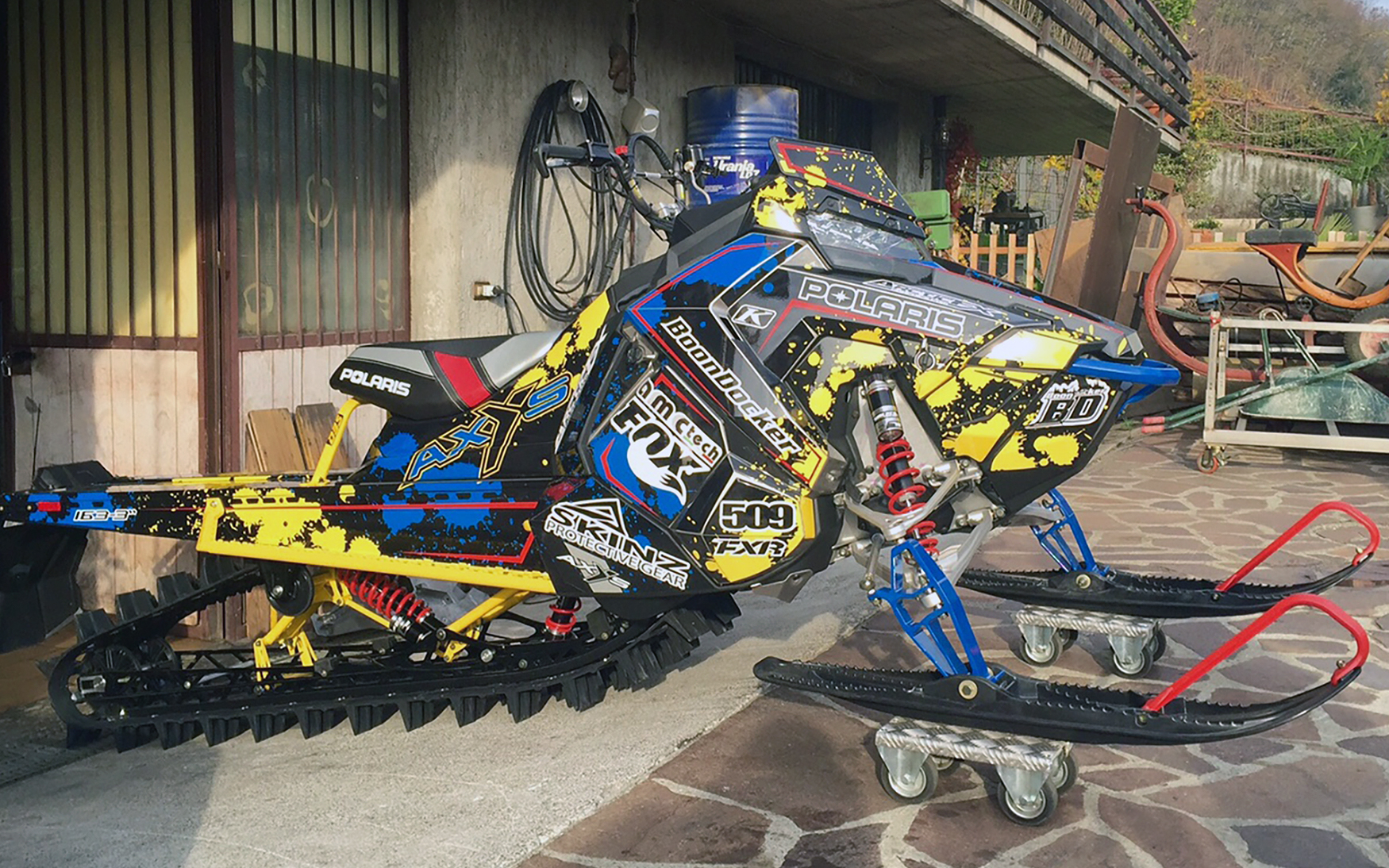 A Polaris Axys Mountain snowmobile with a black, yellow, and blue Paint Splatter custom vinyl wrap.