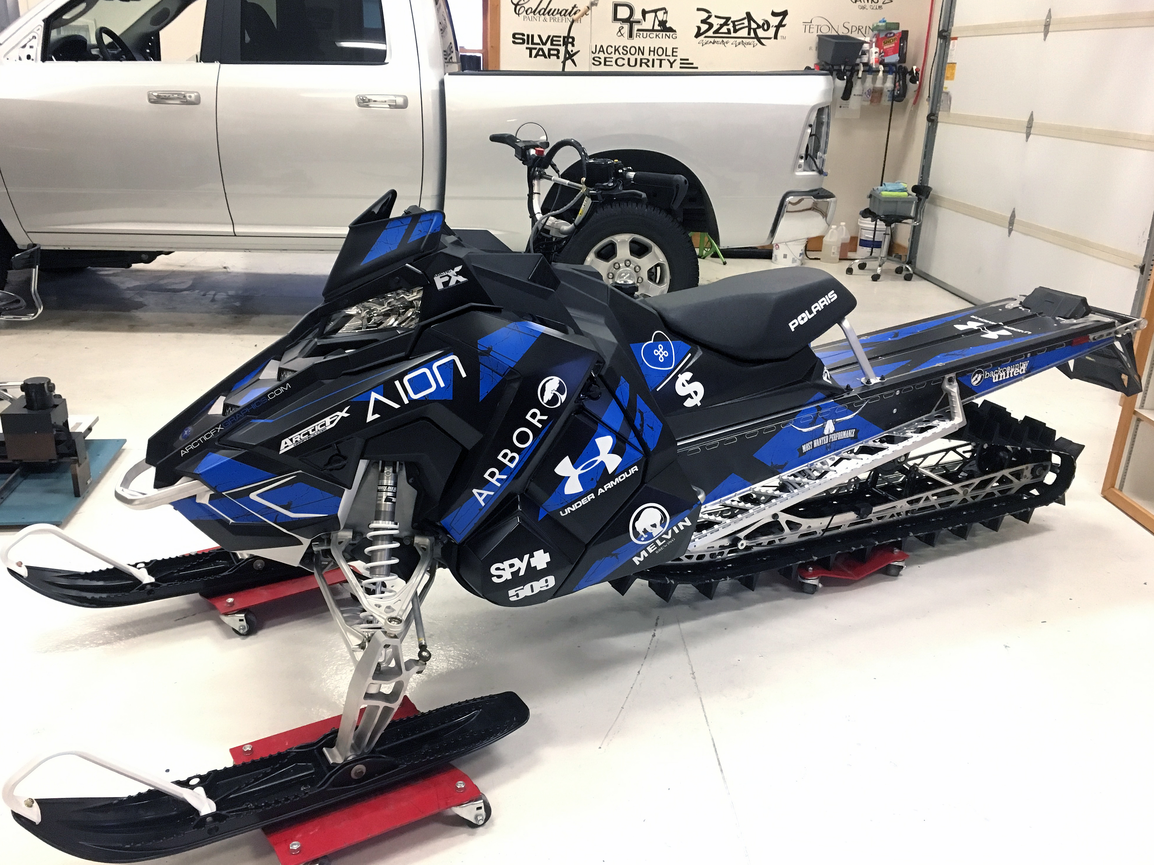 A Polaris Axys Mountain snowmobile with a black, blue, and white Rogue custom vinyl wrap.
