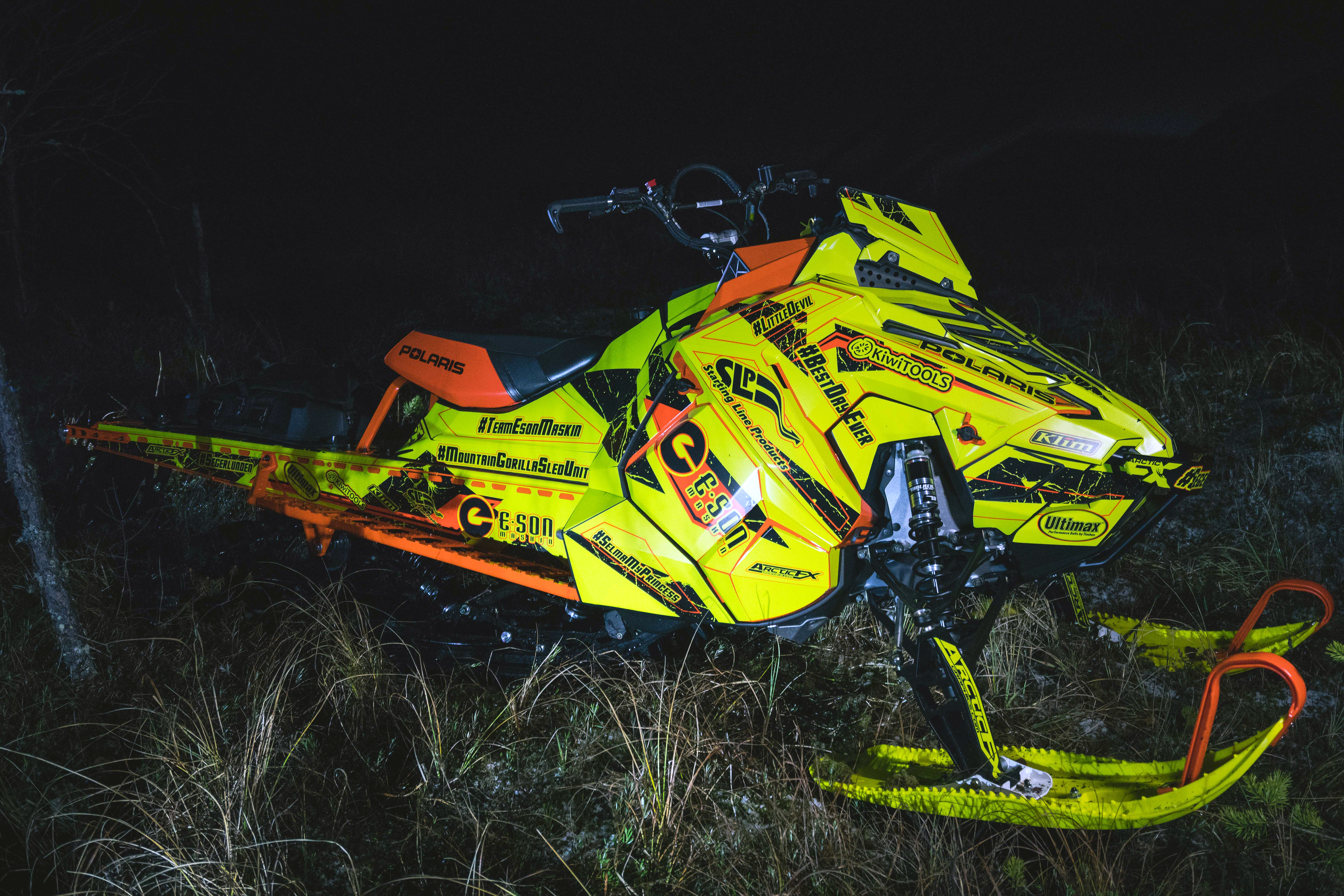 A Polaris Axys Mountain snowmobile with a lime squeeze, black, and orange Rogue custom vinyl wrap.