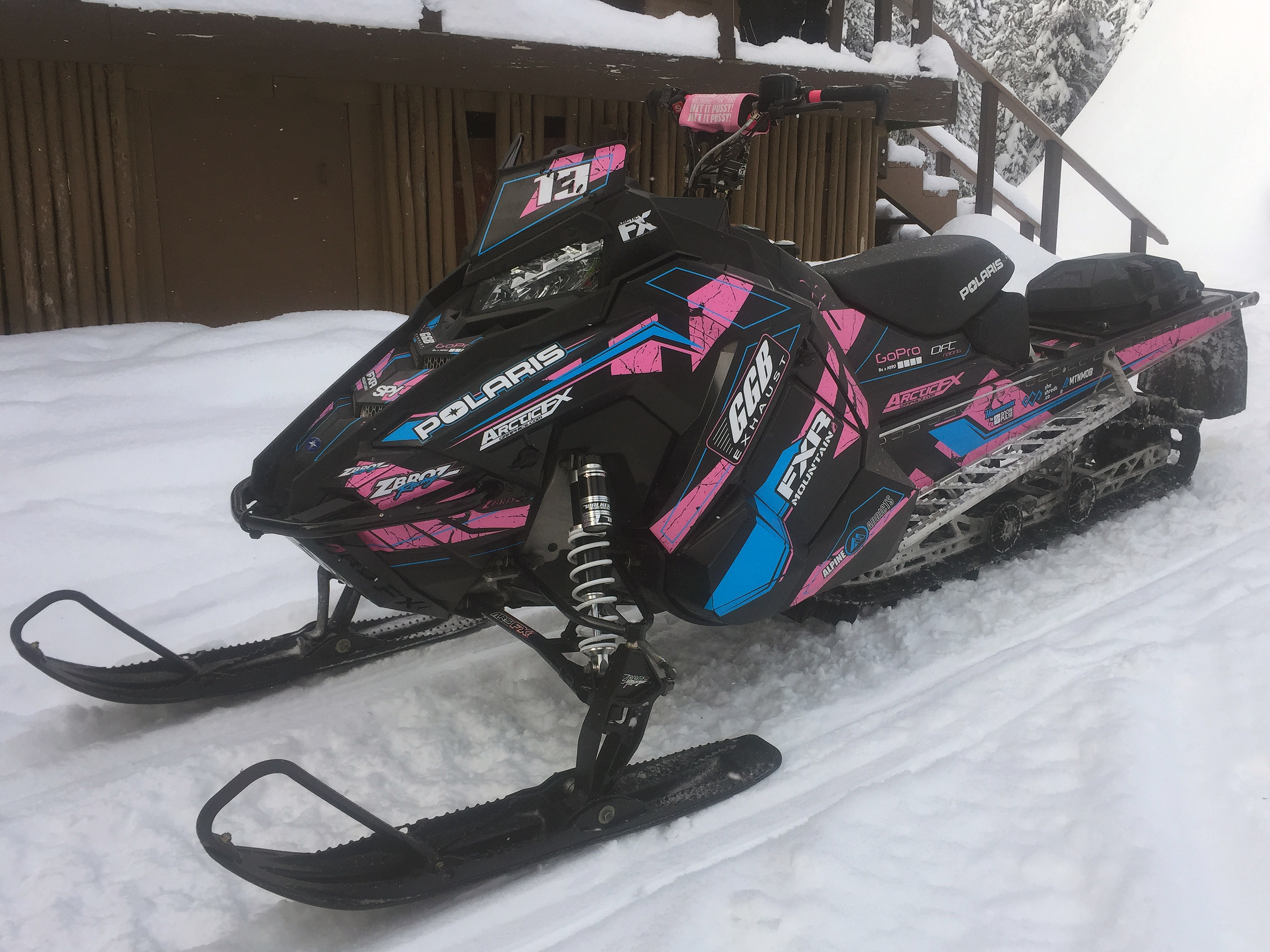 A Polaris Axys Mountain snowmobile with a black, pink, and blue Rogue custom vinyl wrap.