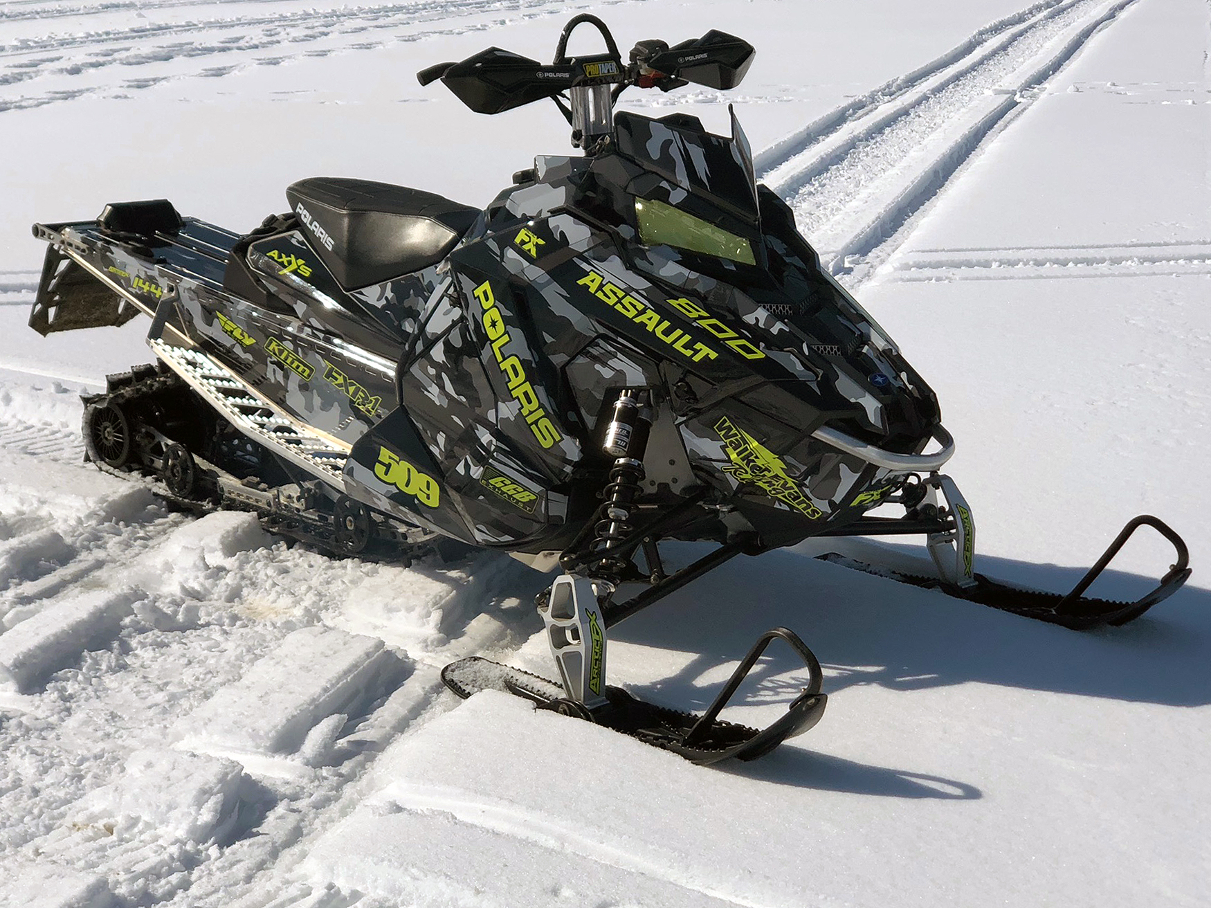 A Polaris Axys Mountain snowmobile with a black, gray, and lime squeeze RR Camo custom vinyl wrap.