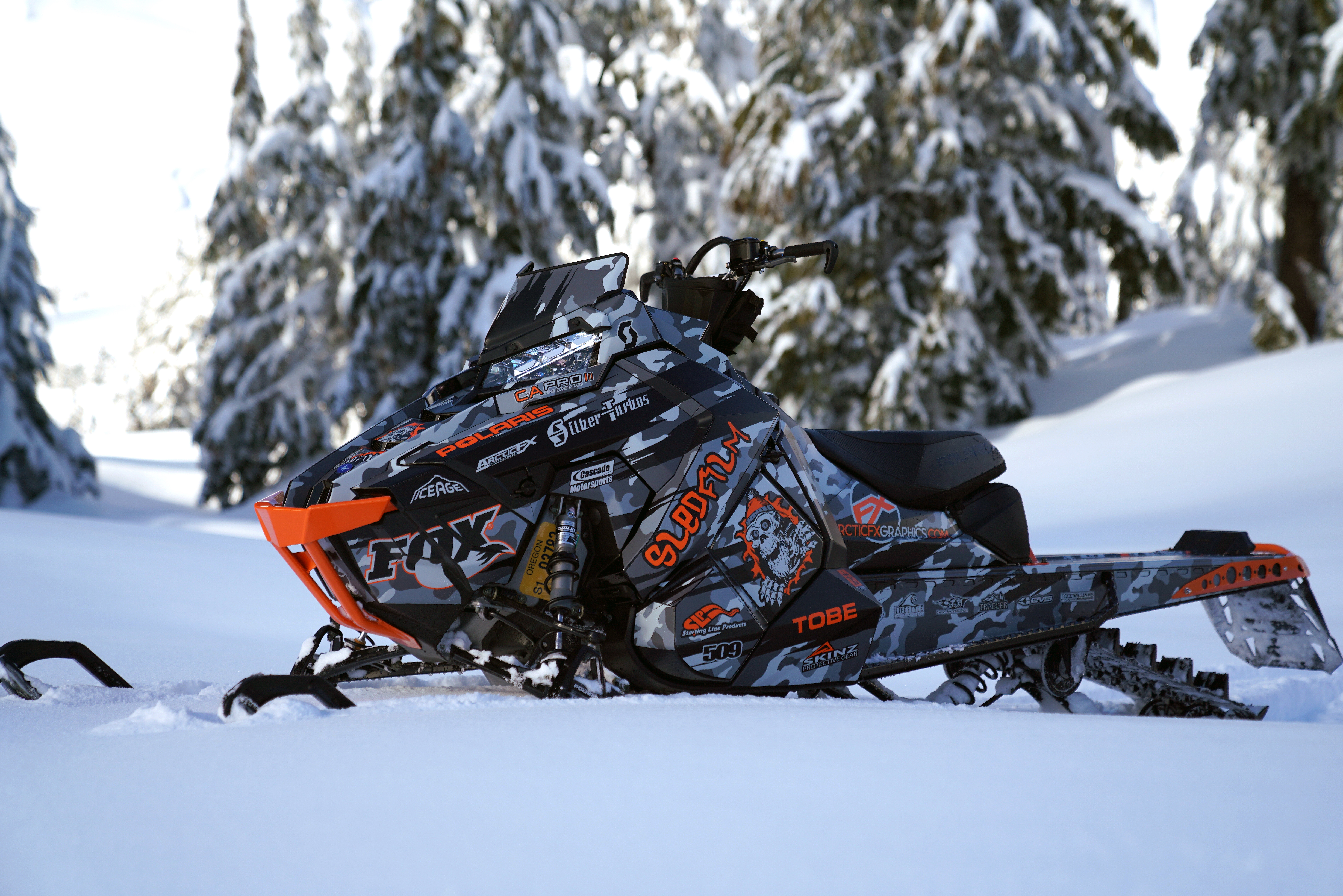 A Polaris Axys Mountain snowmobile with a black, gray, and orange RR Camo custom vinyl wrap.