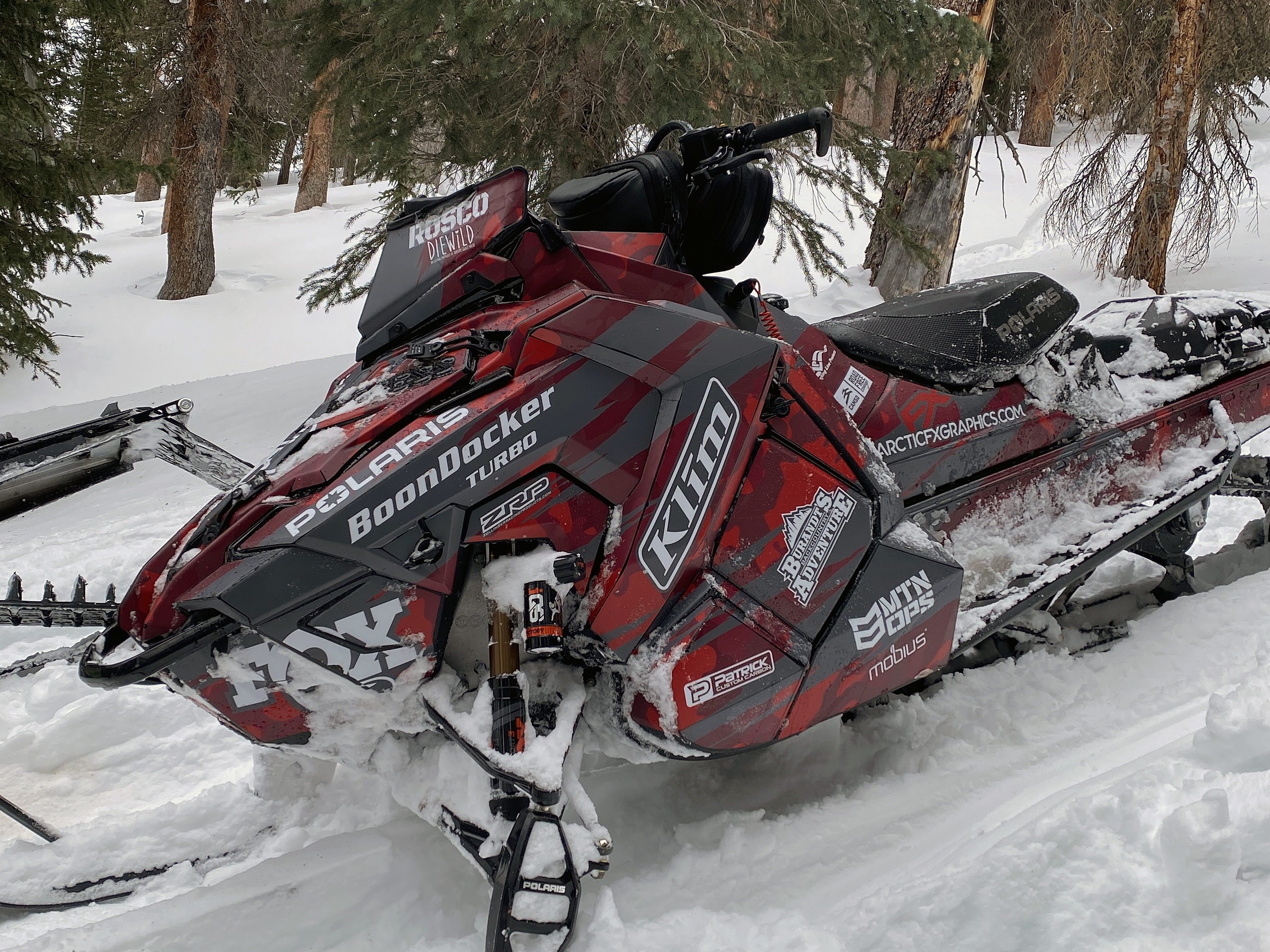 A Polaris Axys Mountain snowmobile with a red, black, and gray RR Camo custom vinyl wrap.