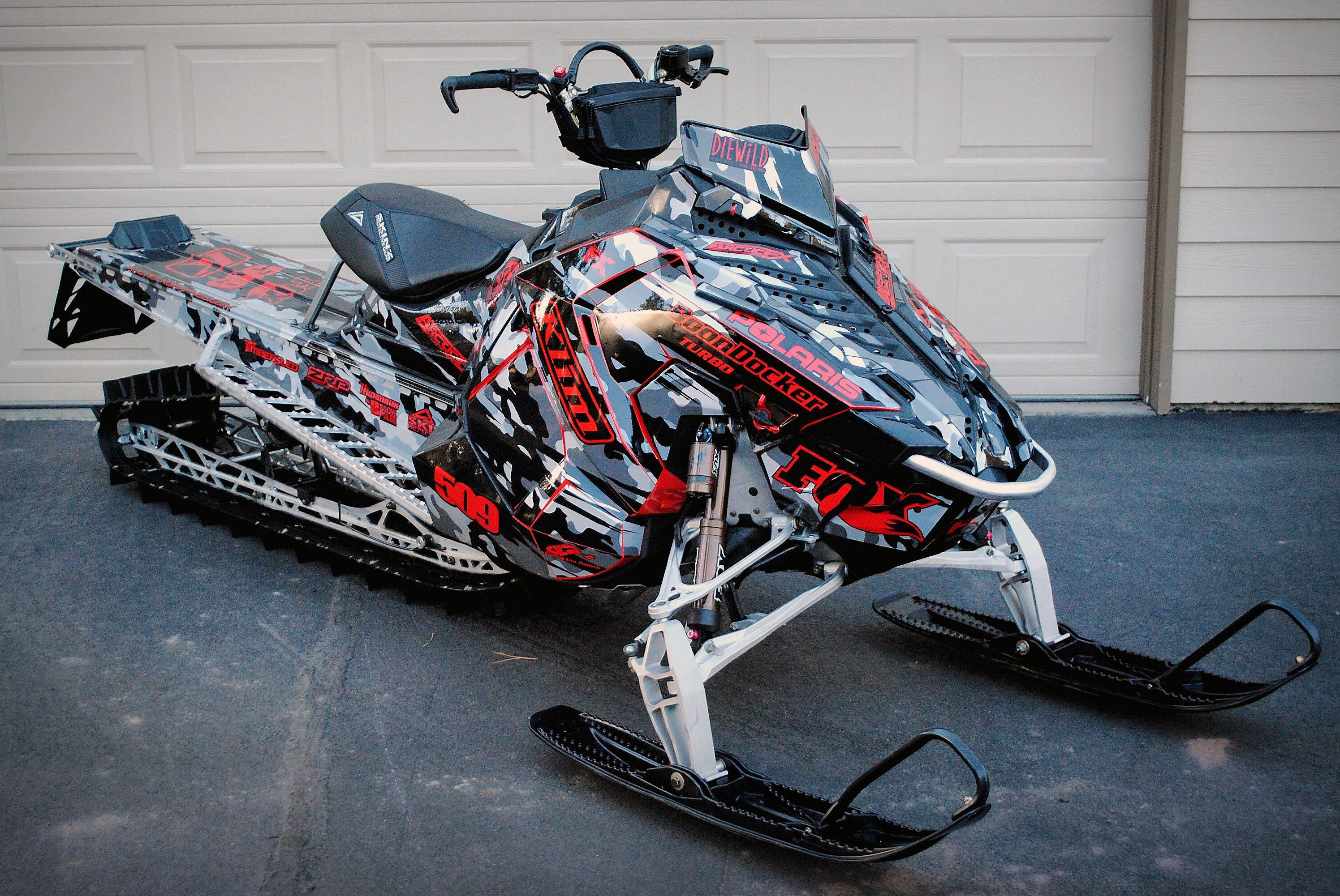 A Polaris Axys Mountain snowmobile with a red, black, and gray RR Camo custom vinyl wrap.