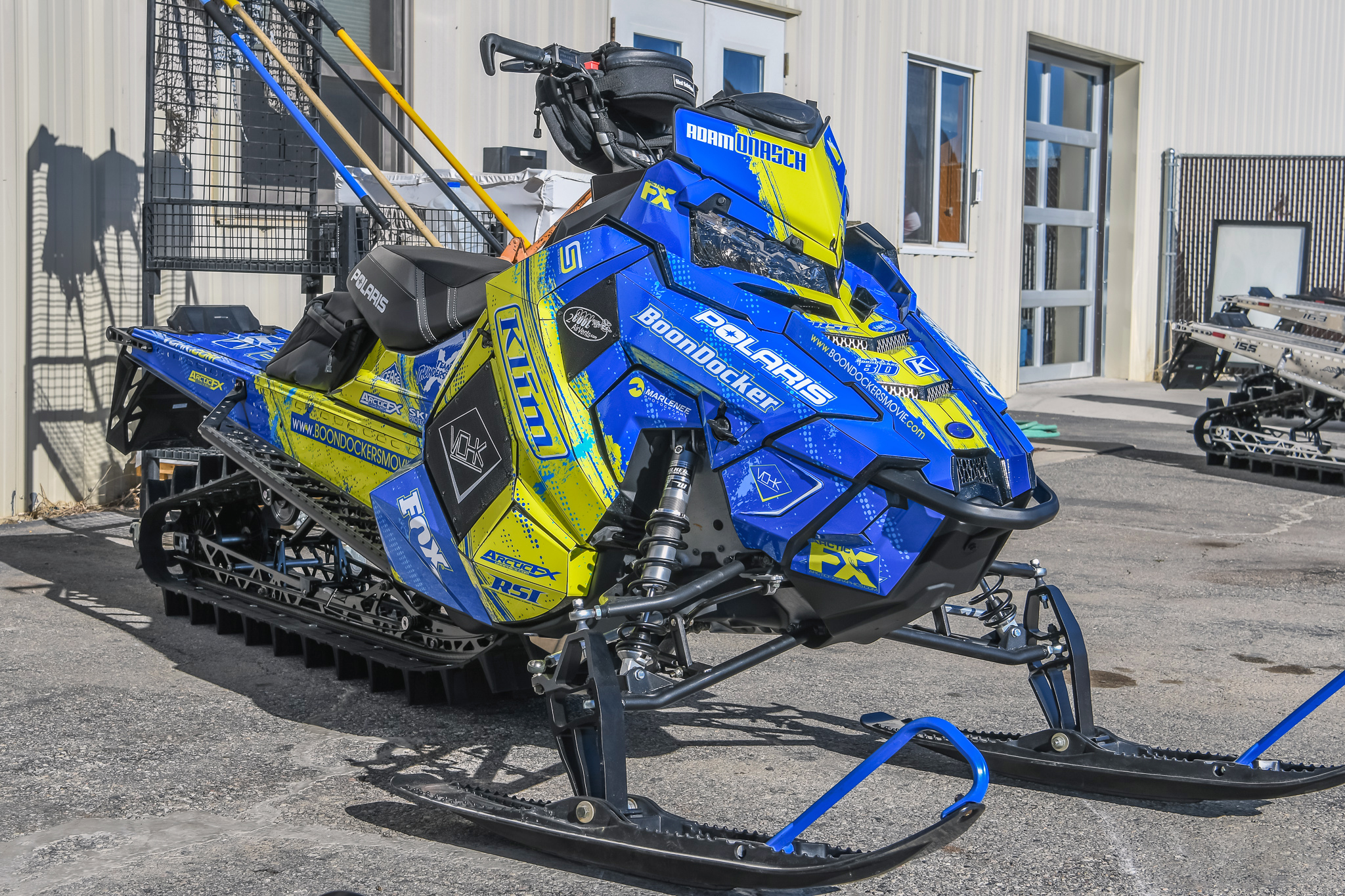 A Polaris Axys Mountain snowmobile with a lime squeeze and blue Sabotage custom vinyl wrap.