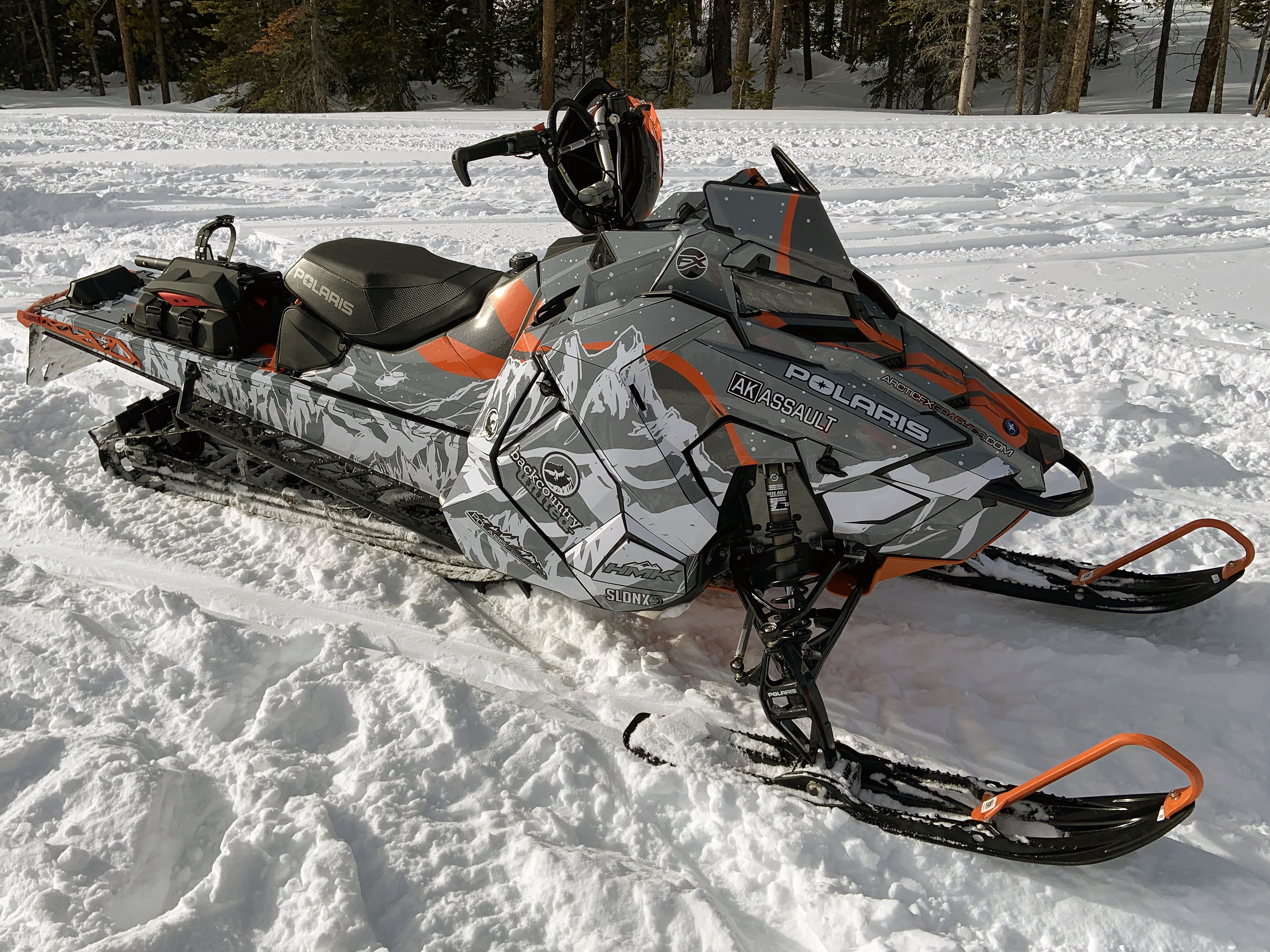 A Polaris Axys Mountain snowmobile with a orange, white, and gray Sherman AK Assault custom vinyl wrap.