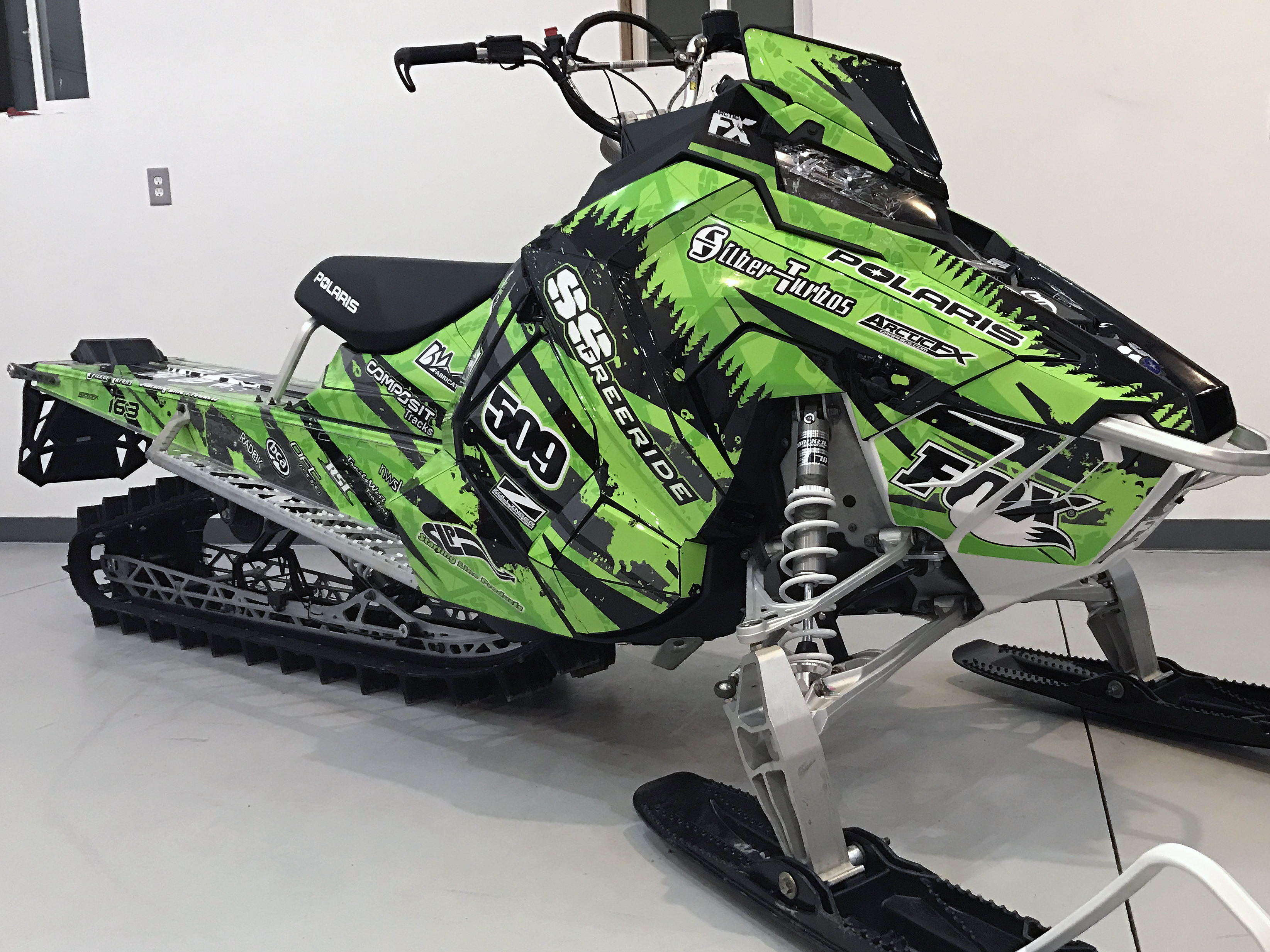 A Polaris Axys Mountain snowmobile with a lime, white, and black Skinner Aftermath custom vinyl wrap.