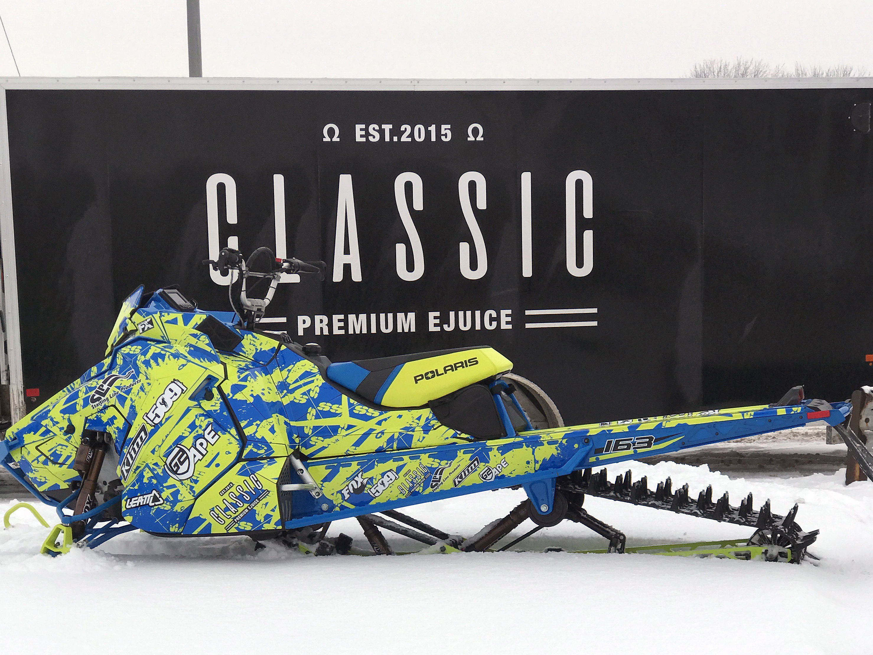 A Polaris Axys Mountain snowmobile with a lime squeeze and blue Skinner Aftermath custom vinyl wrap.