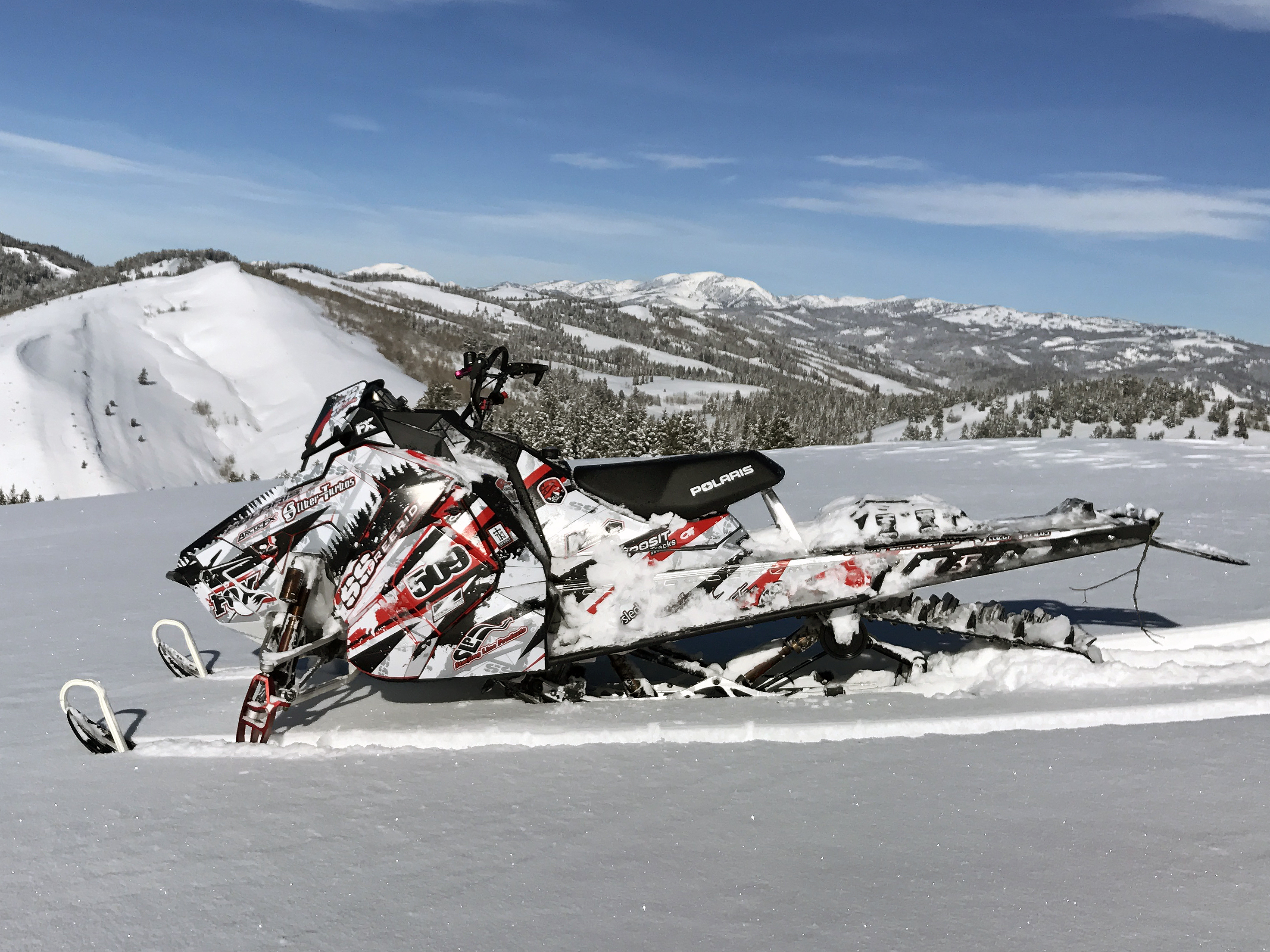 A Polaris Axys Mountain snowmobile with a red, white, and black Skinner Aftermath custom vinyl wrap.