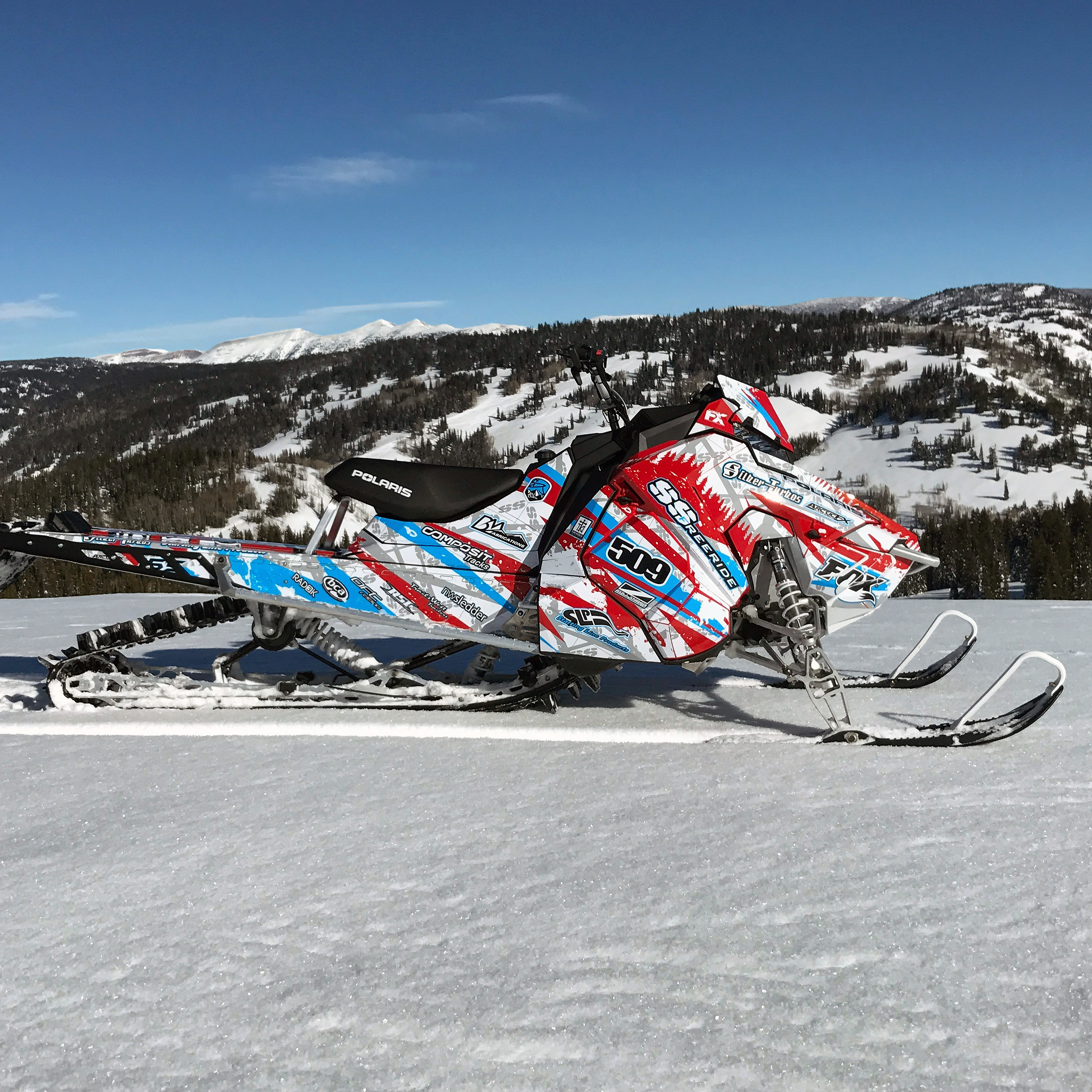 A Polaris Axys Mountain snowmobile with a red, white, and blue Skinner Aftermath custom vinyl wrap.