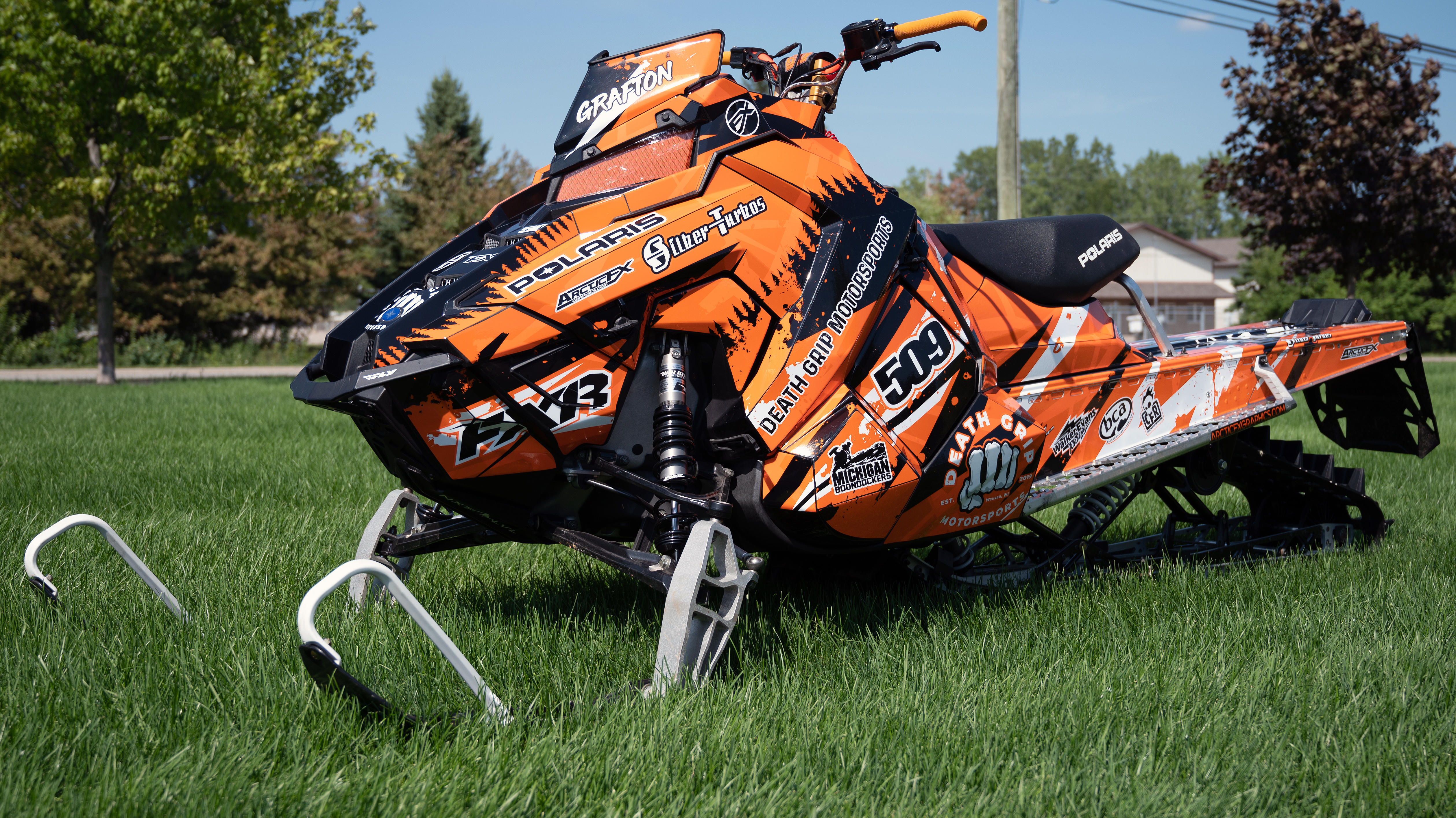 A Polaris Axys Mountain snowmobile with a orange, white, and black Skinner Aftermath custom vinyl wrap.