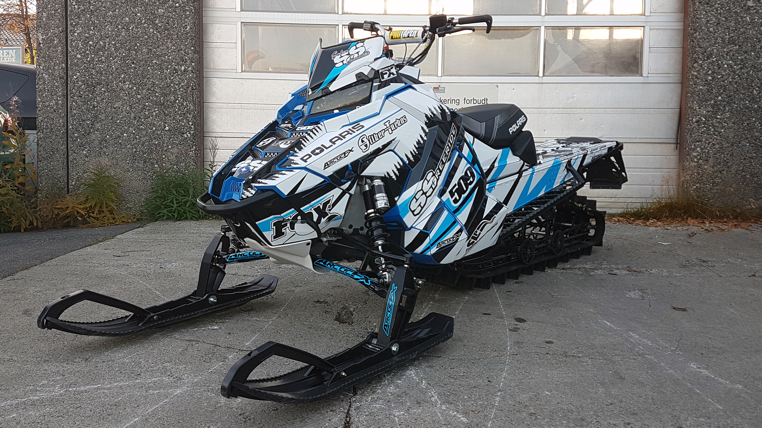 A Polaris Axys Mountain snowmobile with a blue, white, and black Skinner Aftermath custom vinyl wrap.