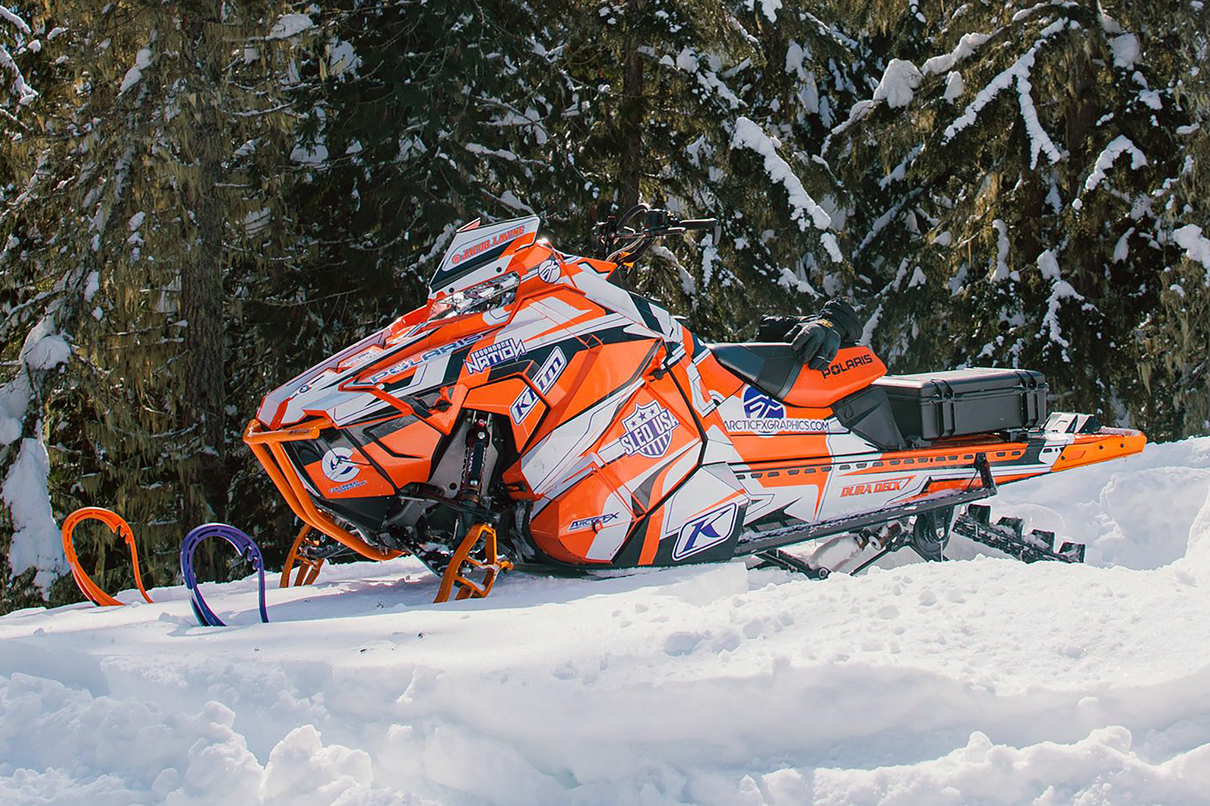 A Polaris Axys Mountain snowmobile with a orange, white, and black Sled USA Inertia custom vinyl wrap.