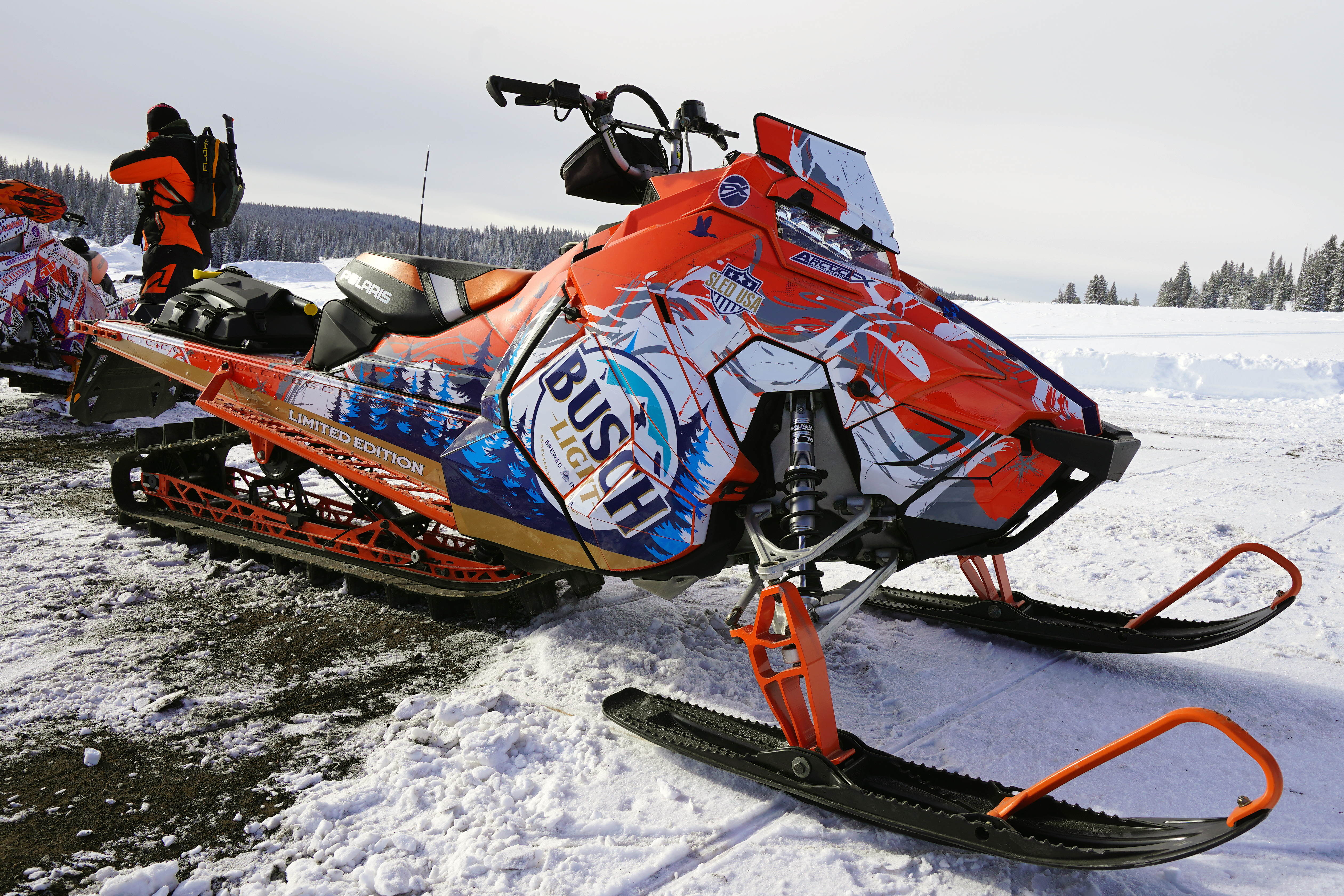 A Polaris Axys Mountain snowmobile with a orange, white, and blue Sub Zero custom vinyl wrap.