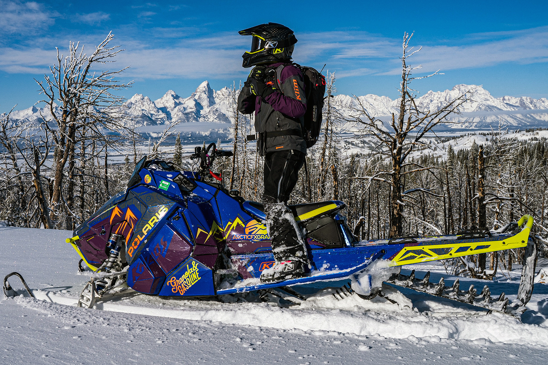 A Polaris Axys Mountain snowmobile with a orange, purple, and blue Teton custom vinyl wrap.