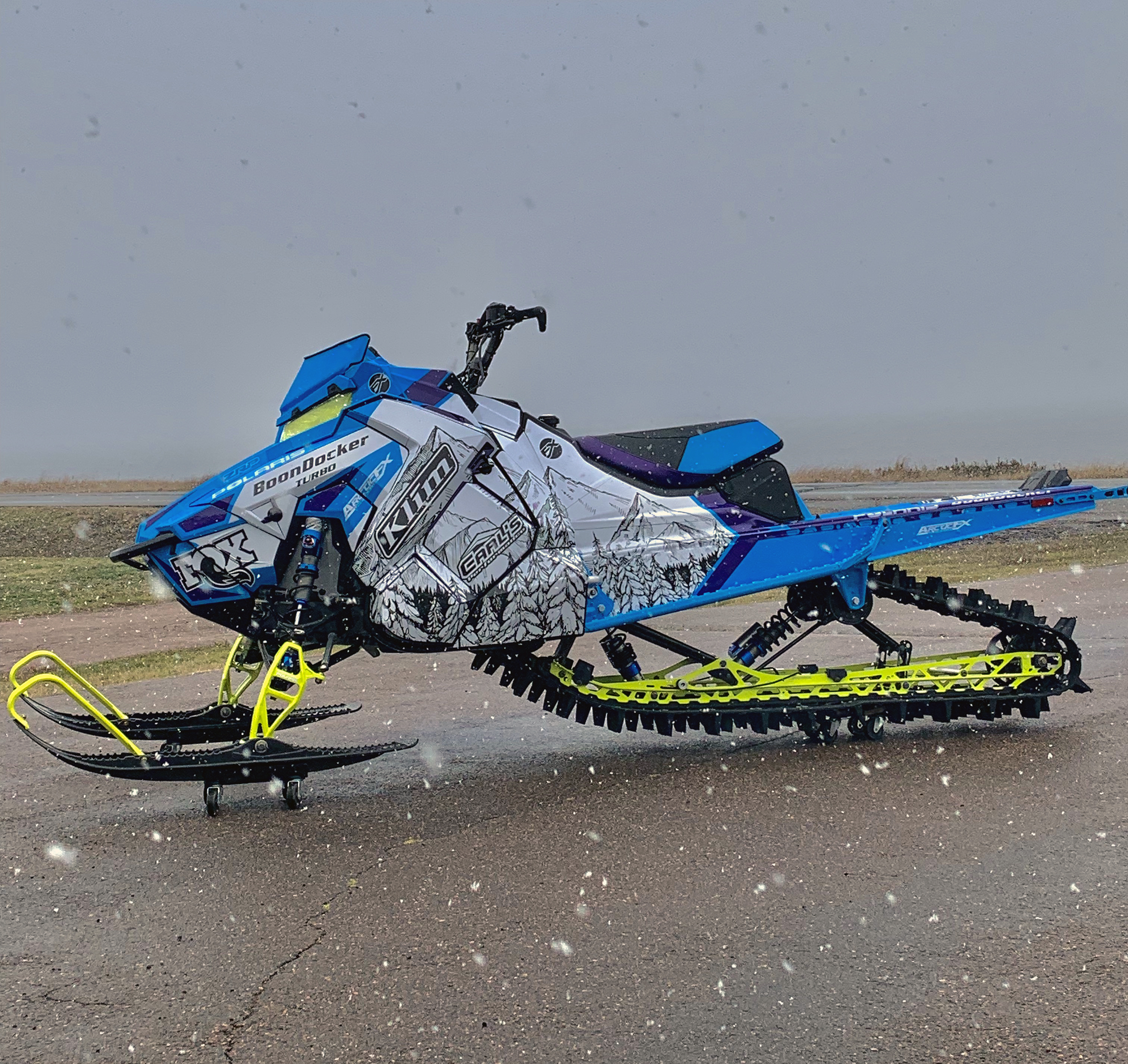 A Polaris Axys Mountain snowmobile with a blue, purple, white, and black Andy Thomas Peaked custom vinyl wrap.