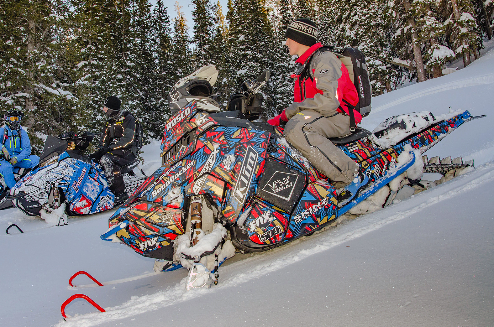 A Polaris Axys Mountain snowmobile with a blue, red, and gold Twisted custom vinyl wrap.