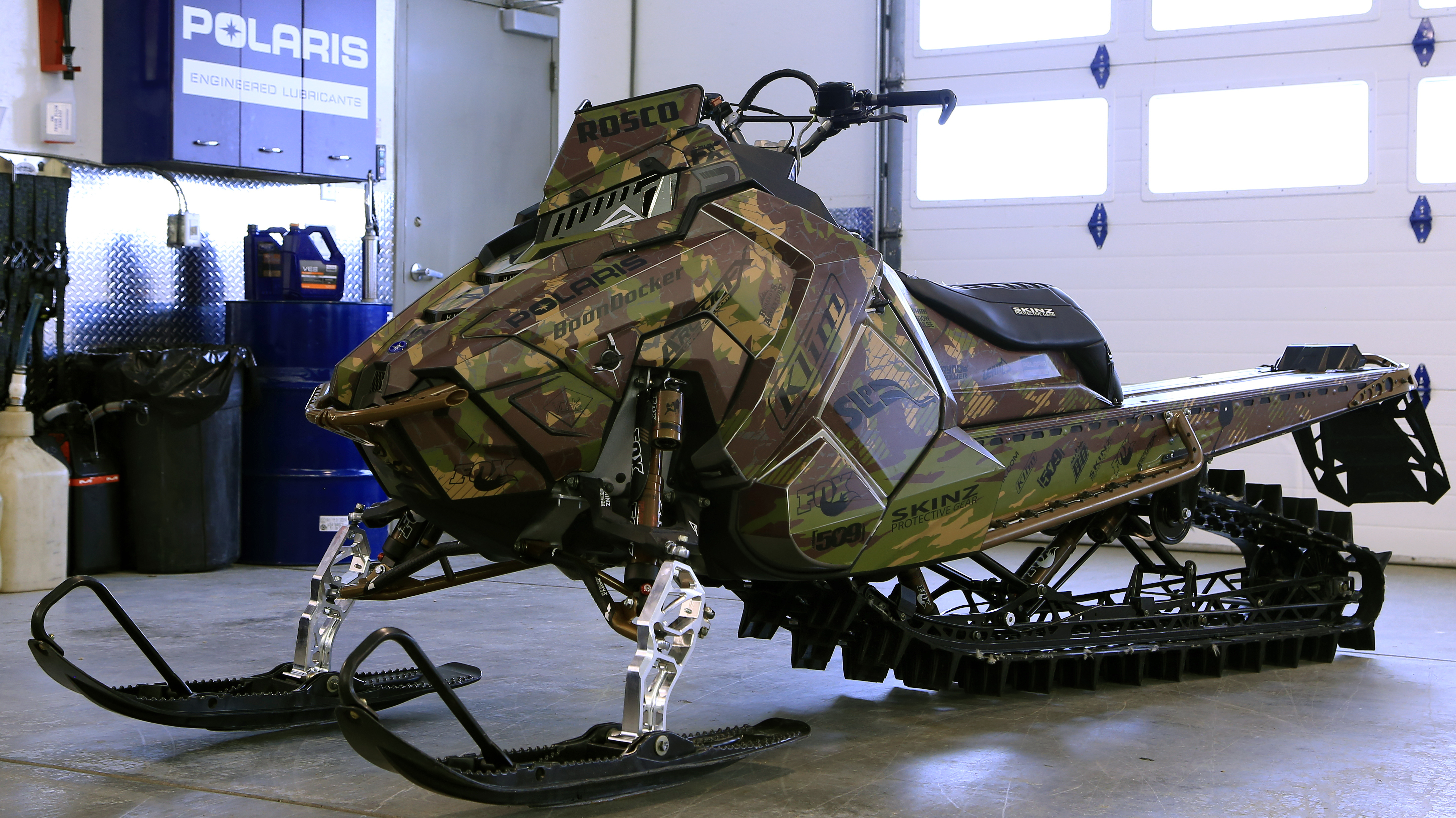 A Polaris Axys Mountain snowmobile with a army green, brown, and tan Urban Camo custom vinyl wrap.
