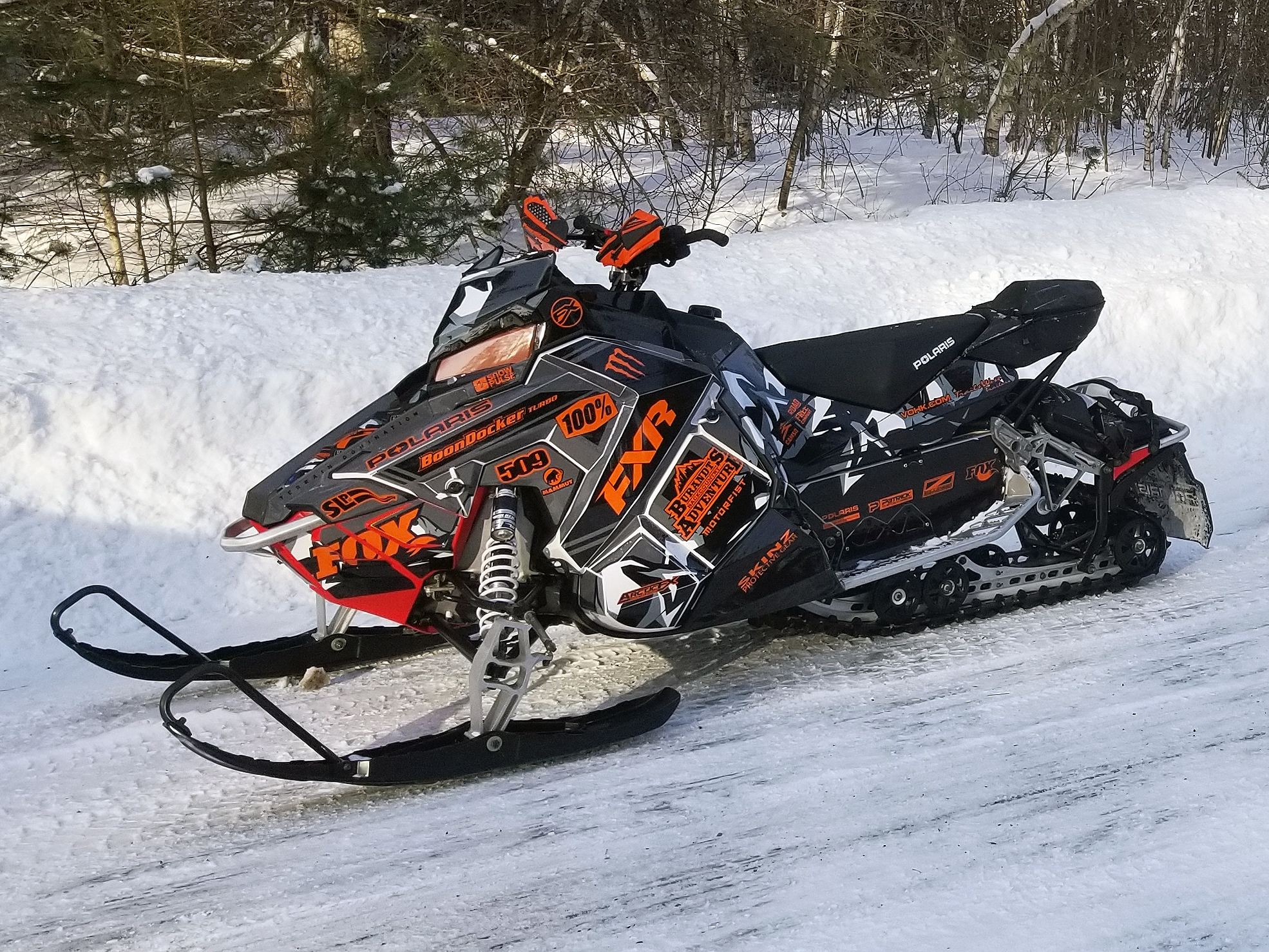 A Polaris Axys Trail snowmobile with a black, white, and orange Burandt Vista custom vinyl wrap.