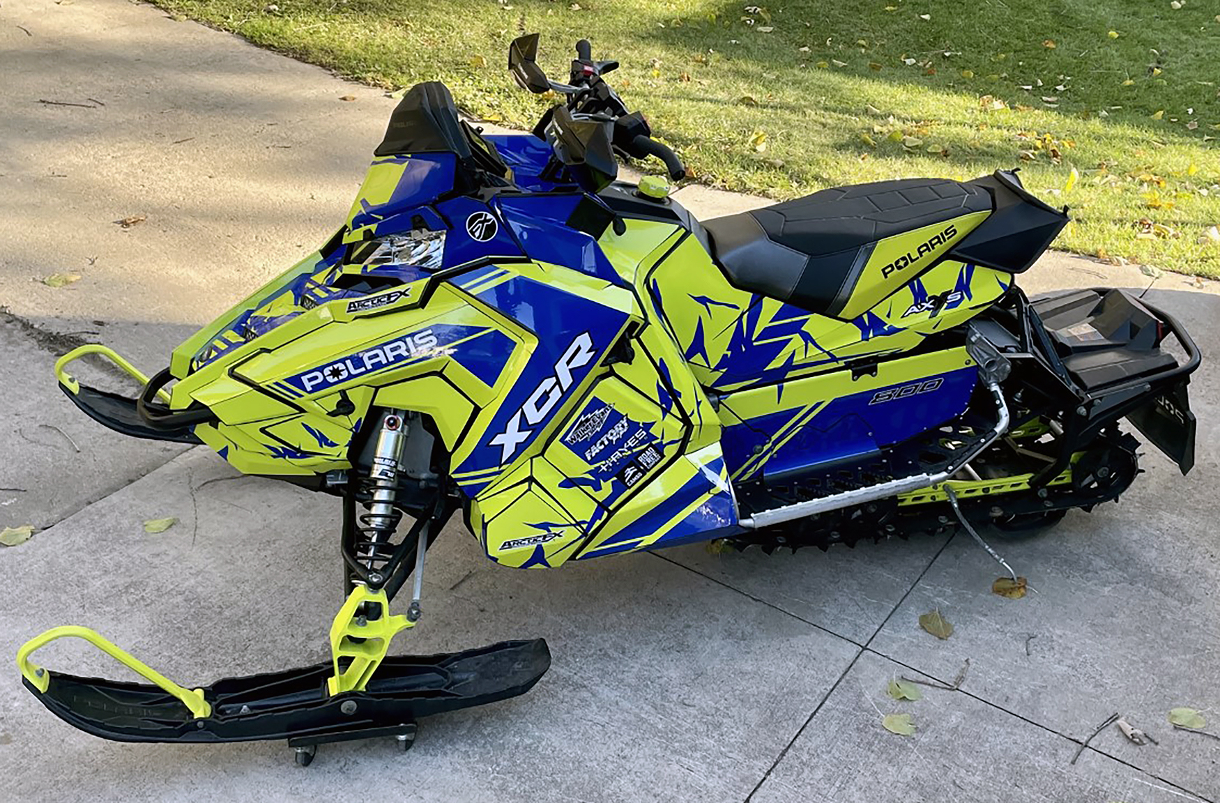A Polaris Axys Trail snowmobile with a black, blue, and lime squeeze Burandt Vista custom vinyl wrap.