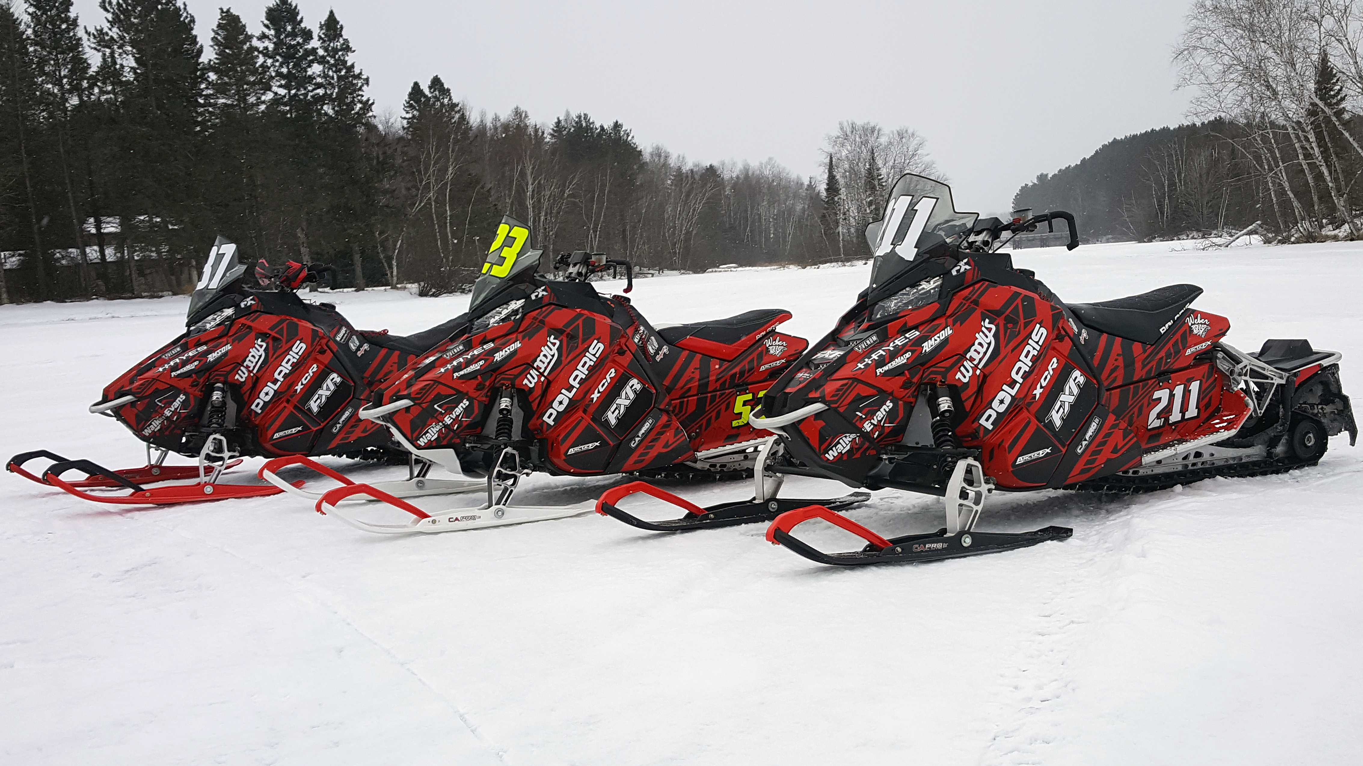Three Polaris Axys Trail snowmobiles with black, white, and red stripes Evasion custom vinyl wraps.