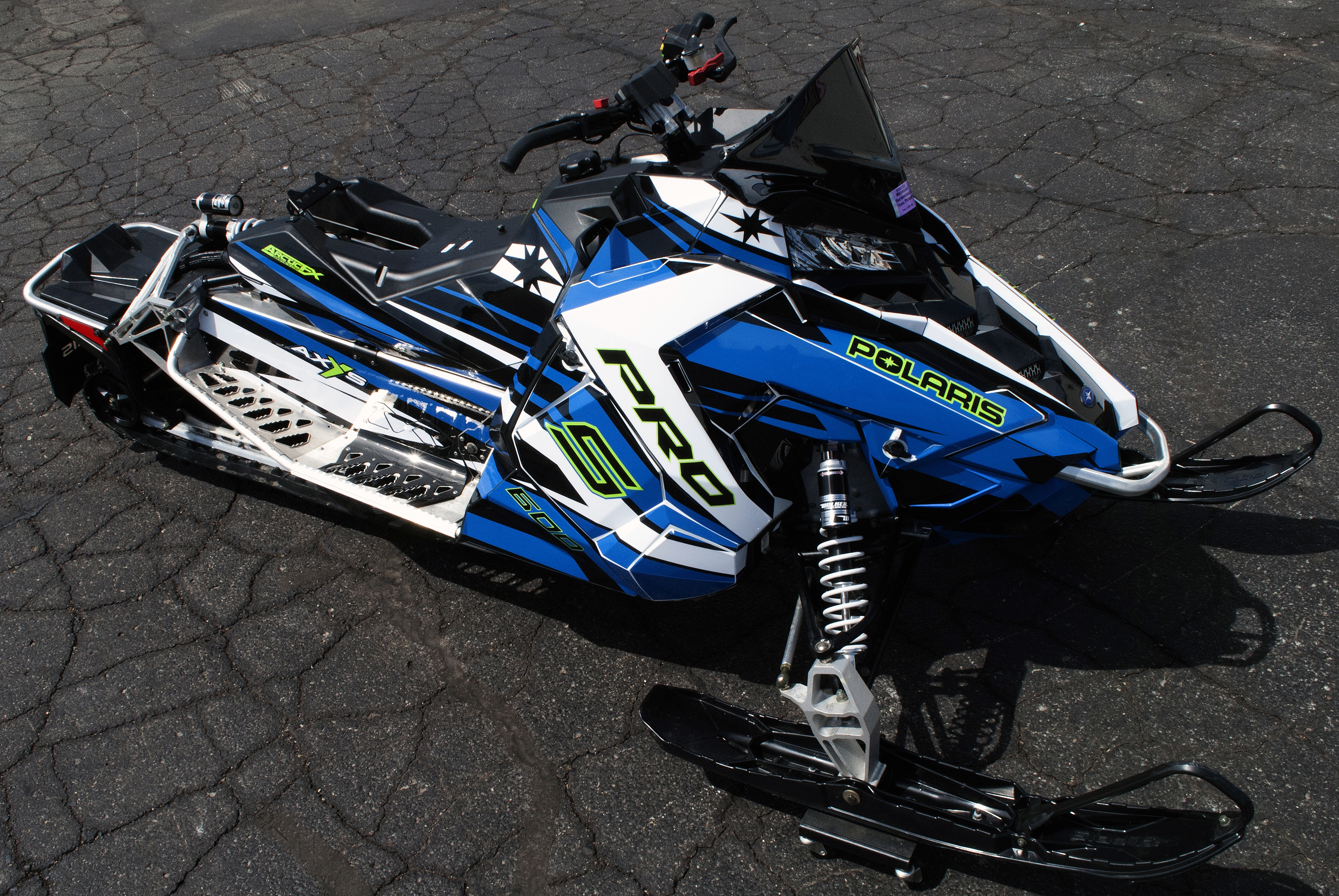 A Polaris Axys Trail snowmobile with a black, white, lime, and blue racing stripes Relay custom vinyl wrap.