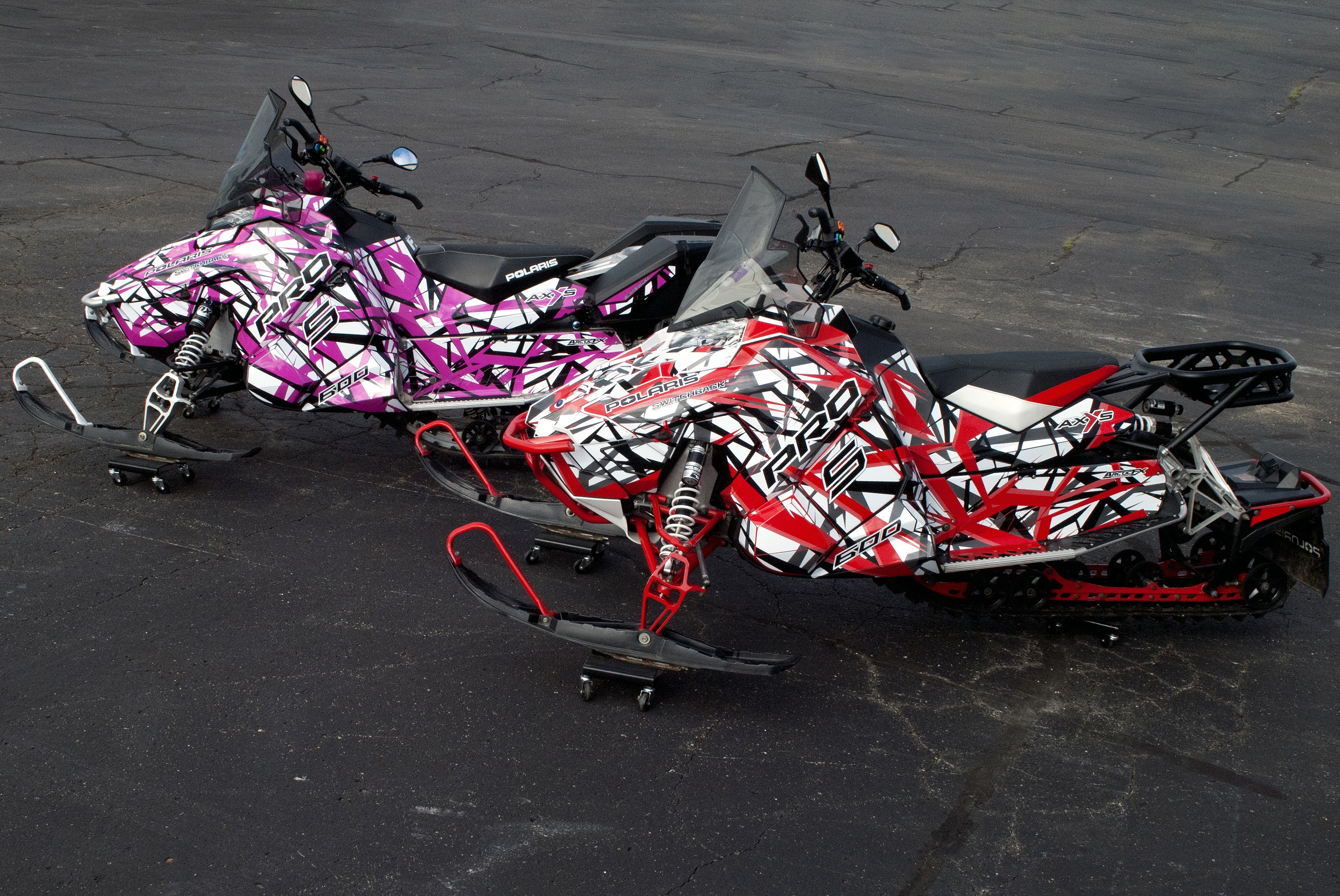 Two Polaris Axys Trail snowmobiles with black, white, red, and pink stripes Shattered Illusion custom vinyl wraps.