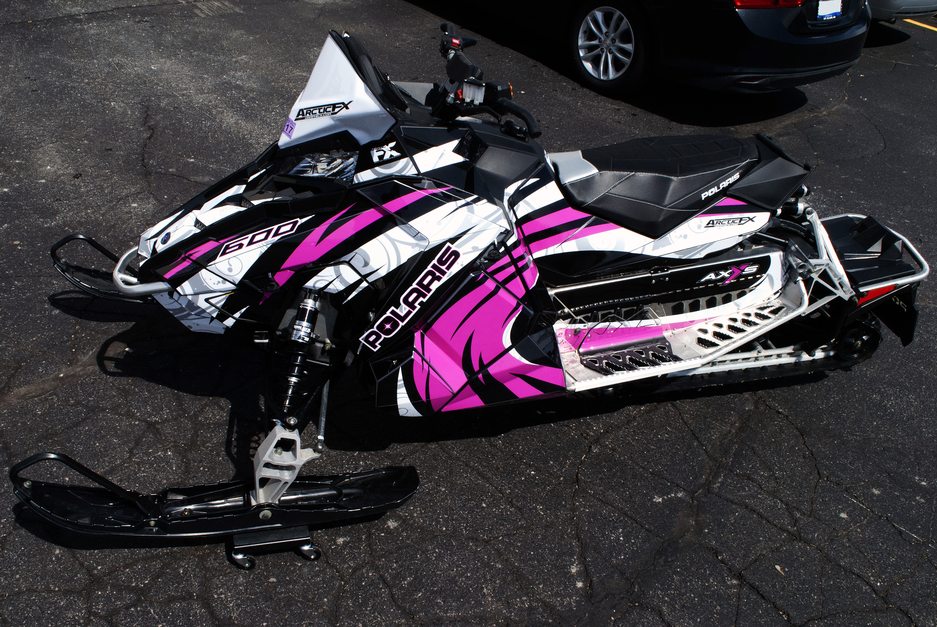 A Polaris Axys Trail snowmobile with a black, pink, gray, and white Surge custom vinyl wrap.