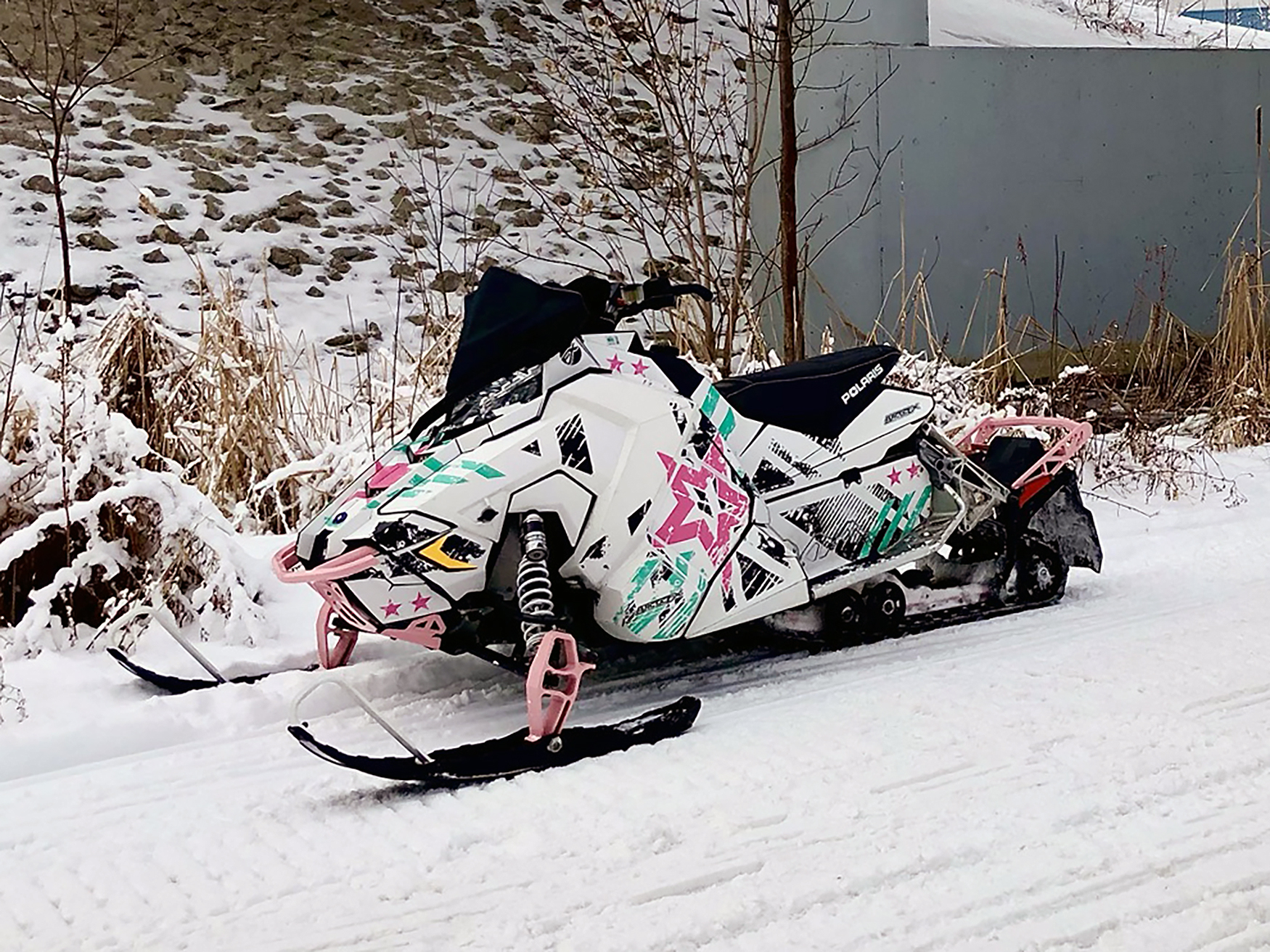 A Polaris Axys Trail snowmobile with a aqua, pink, and black Wartorn custom vinyl wrap.