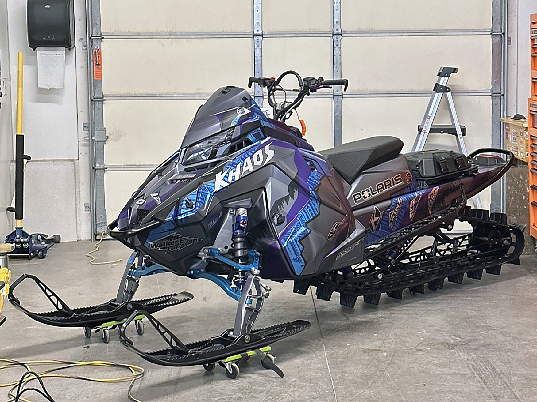 A Polaris Matryx Mountain snowmobile with a chrome, blue, purple, and black Adams Alpine custom vinyl wrap.