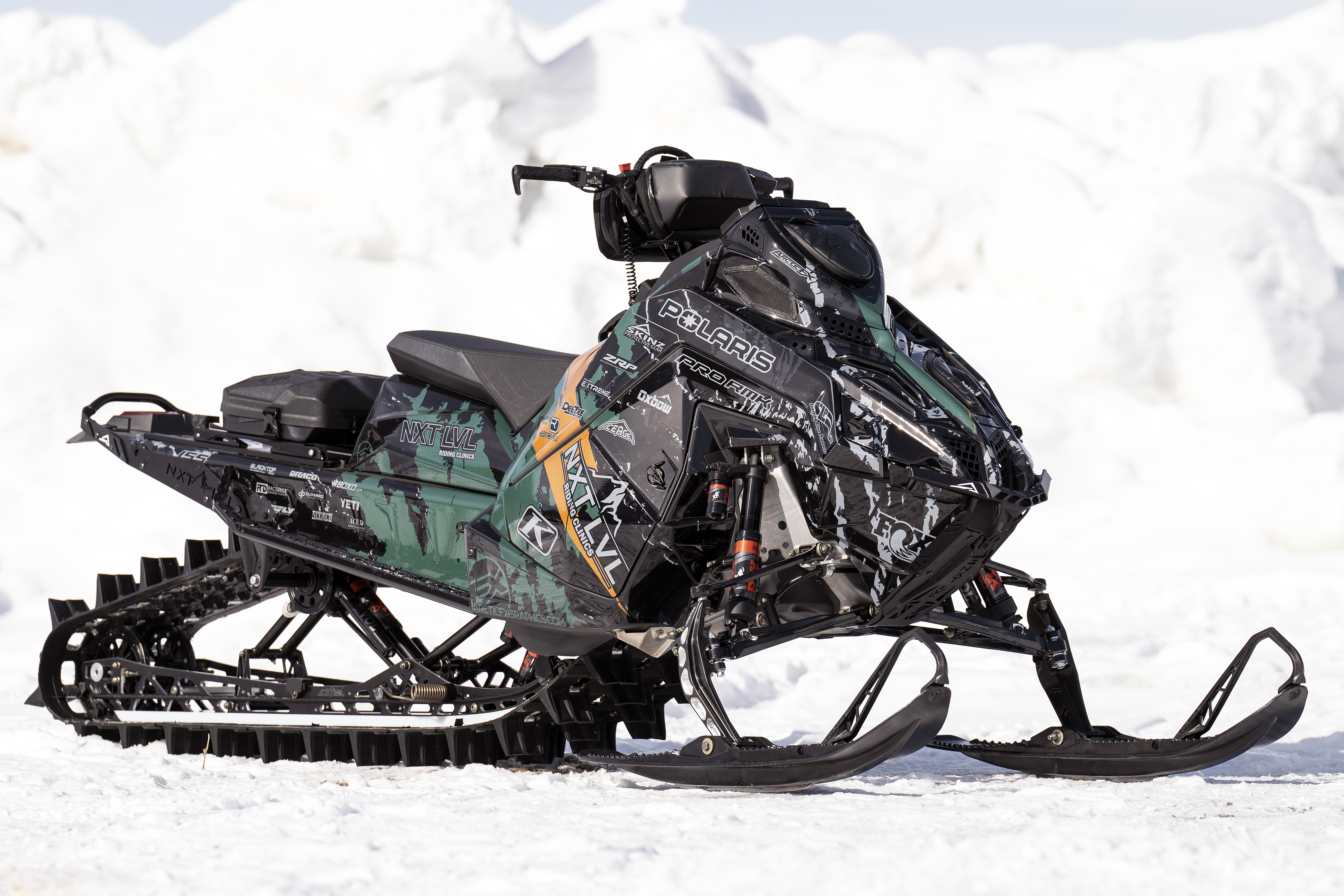 A Polaris Matryx Mountain snowmobile with a green, orange, black, and gray Adams Inversion custom vinyl wrap.
