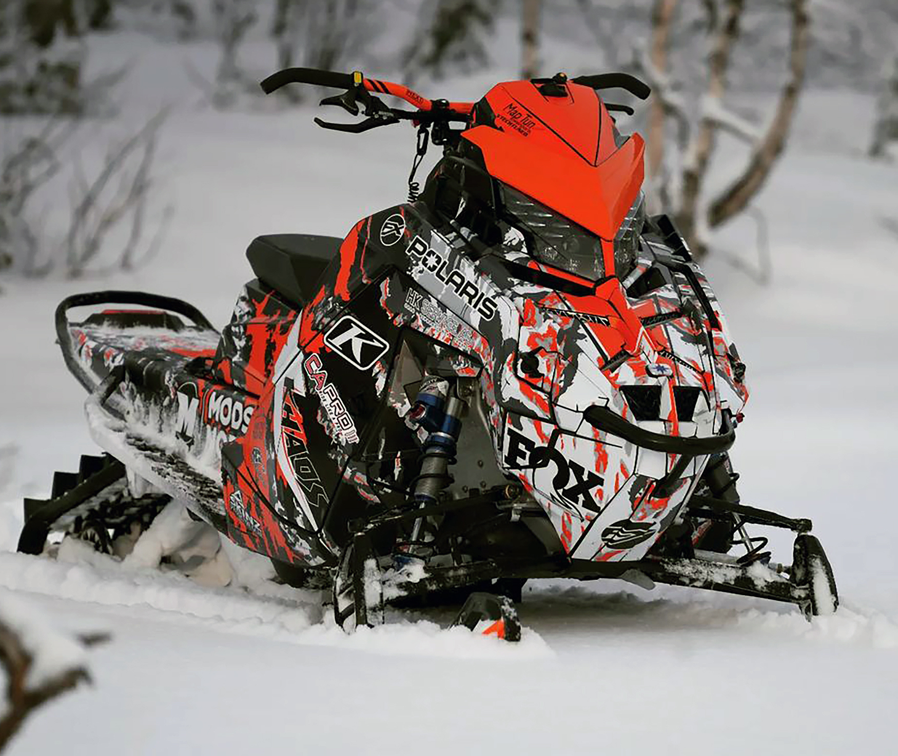 A Polaris Matryx Mountain snowmobile with a orange, black, and white Adams Inversion custom vinyl wrap.
