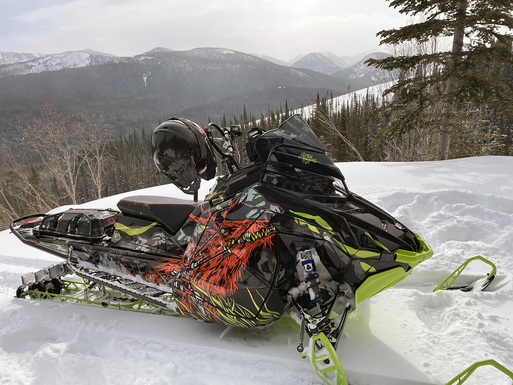A Polaris Matryx Mountain snowmobile with a chrome, black, orange, and lime squeeze Leif Alvarsson Specter custom vinyl wrap.