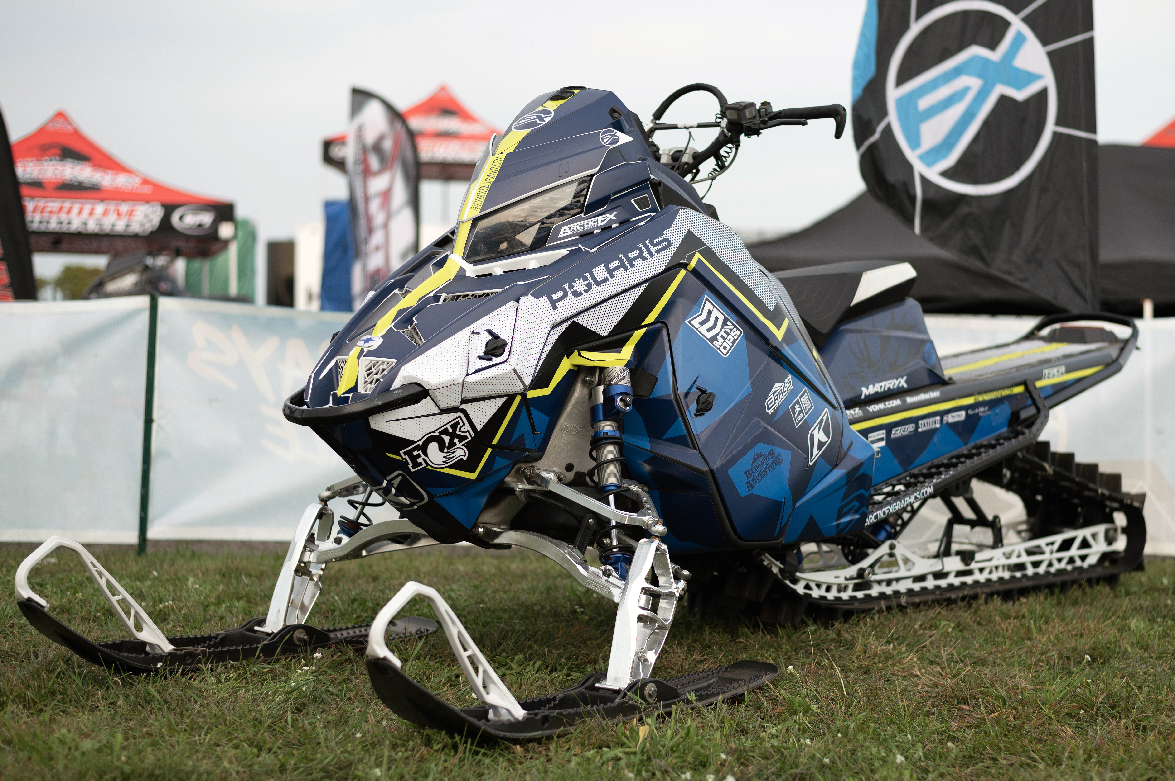 A Polaris Matryx Mountain snowmobile with a white, blue, and lime squeeze Burandt Incognito custom vinyl wrap.