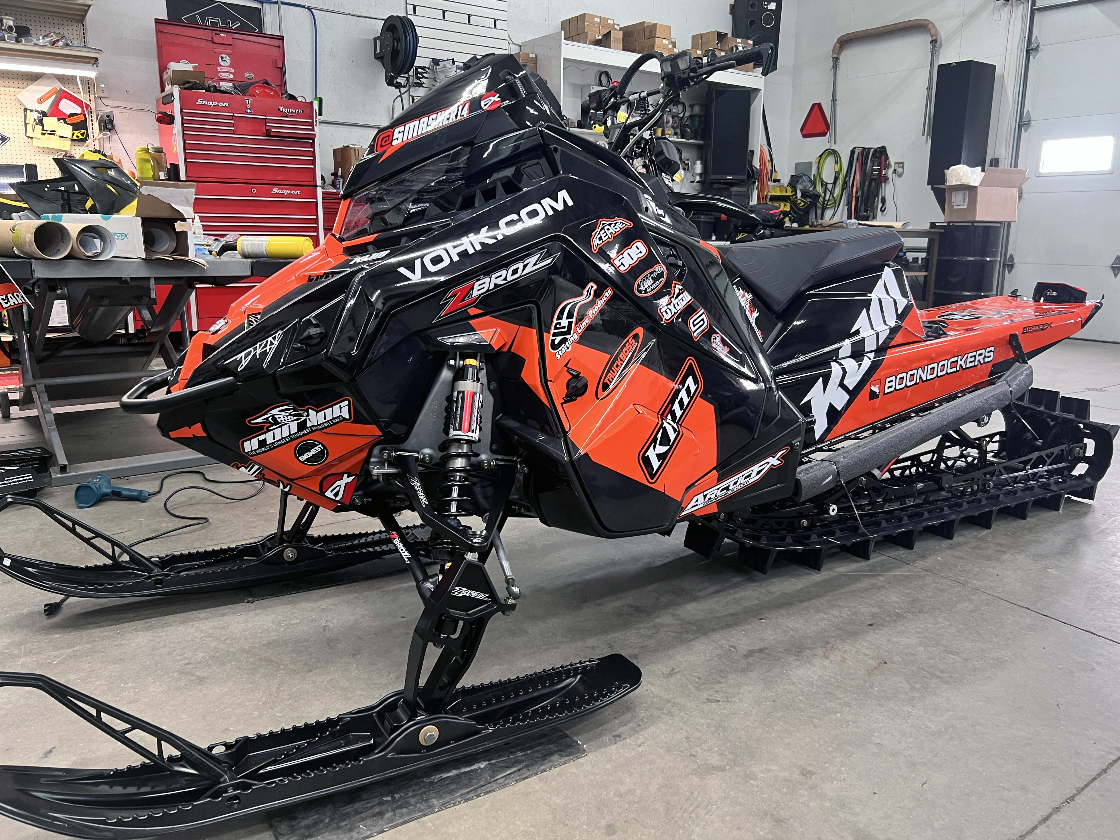 A Polaris Matryx Mountain snowmobile with a orange and black Klim F5 Ion custom vinyl wrap.