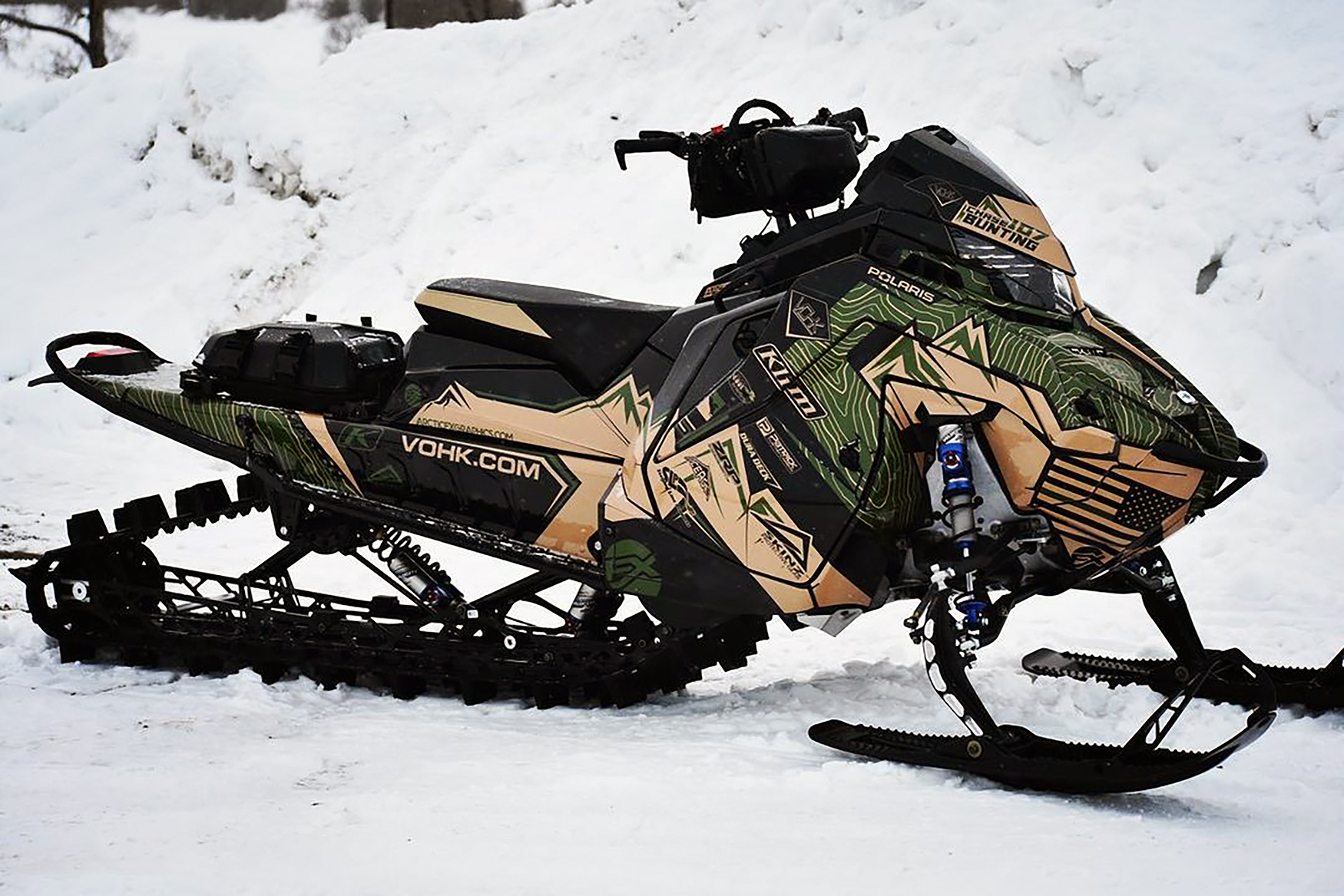 A Polaris Matryx Mountain snowmobile with a beige, army green, and black Teton custom vinyl wrap.