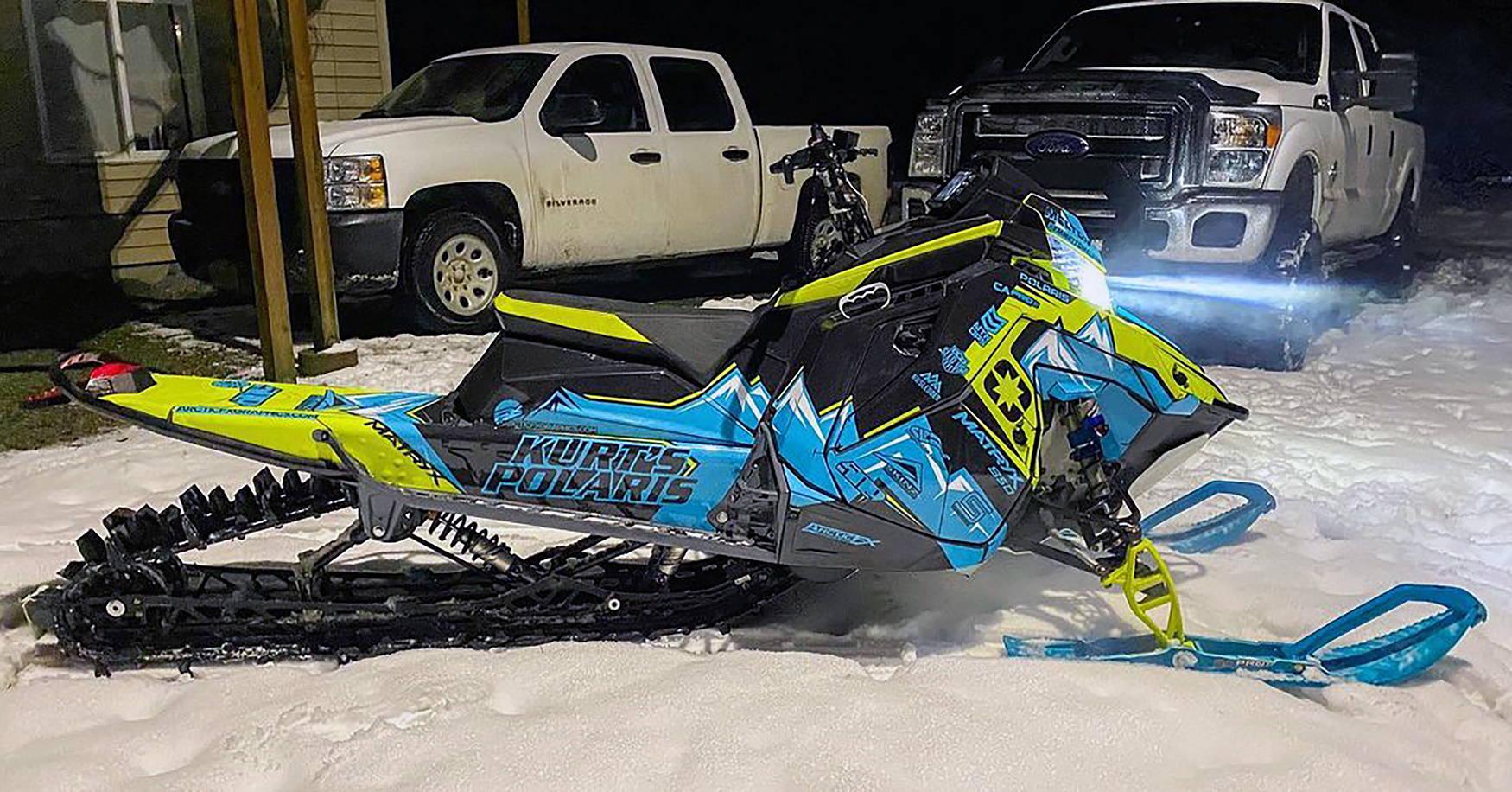 A Polaris Matryx Mountain snowmobile with a blue, lime squeeze, and black Teton custom vinyl wrap.