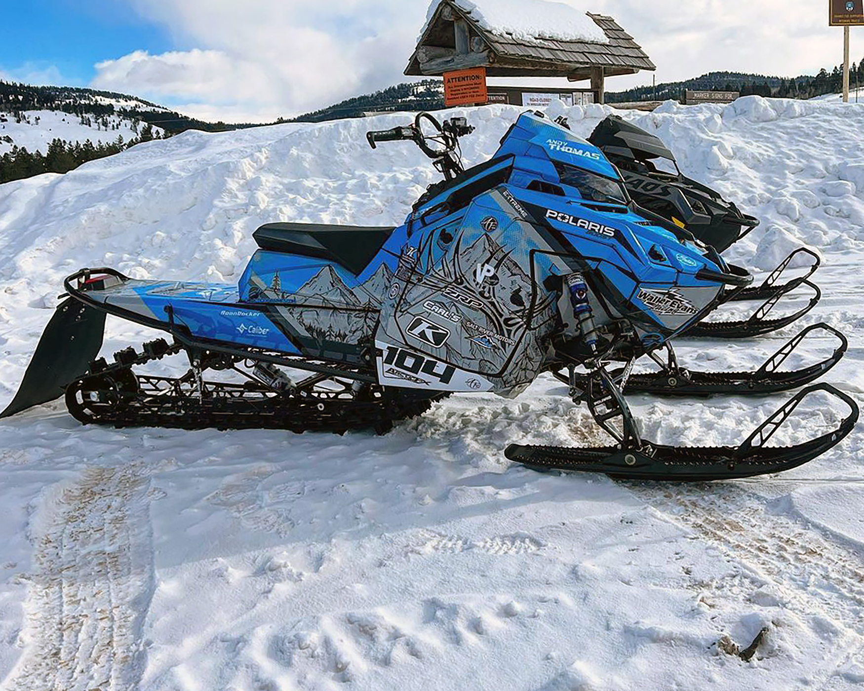 A Polaris Matryx Mountain snowmobile with a blue, gray, and black Andy Thomas Attack custom vinyl wrap.