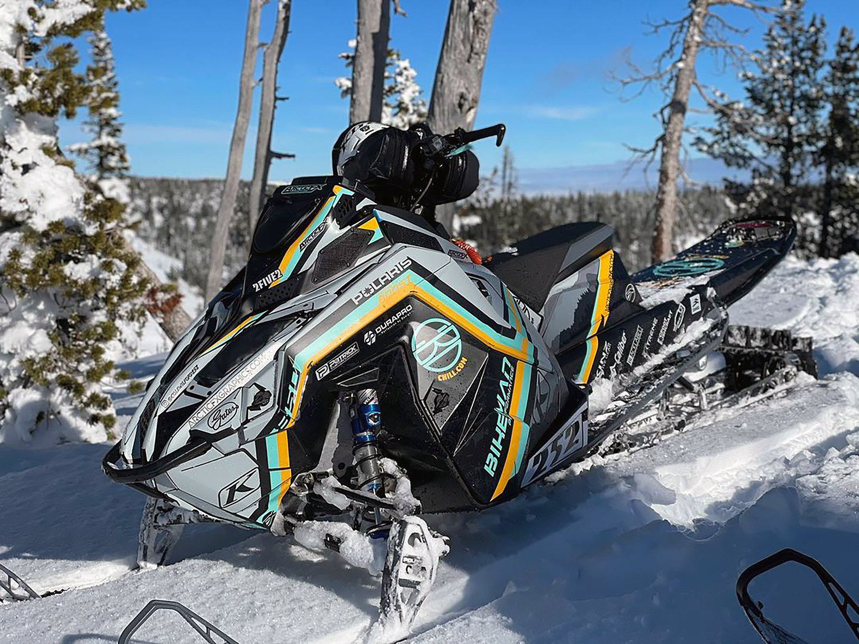 A Polaris Matryx Mountain snowmobile with a black, aqua, and yellow Wilford Chilled custom vinyl wrap.