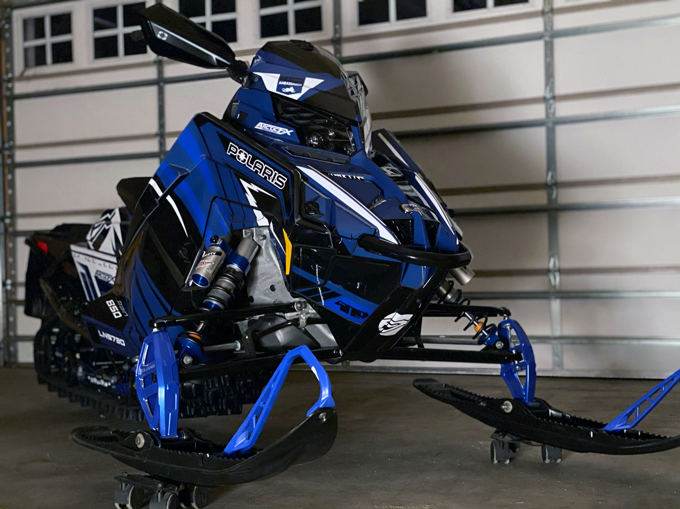 A Polaris Matryx Trail snowmobile with a white, blue, and black Kesterke Adrenaline custom vinyl wrap.