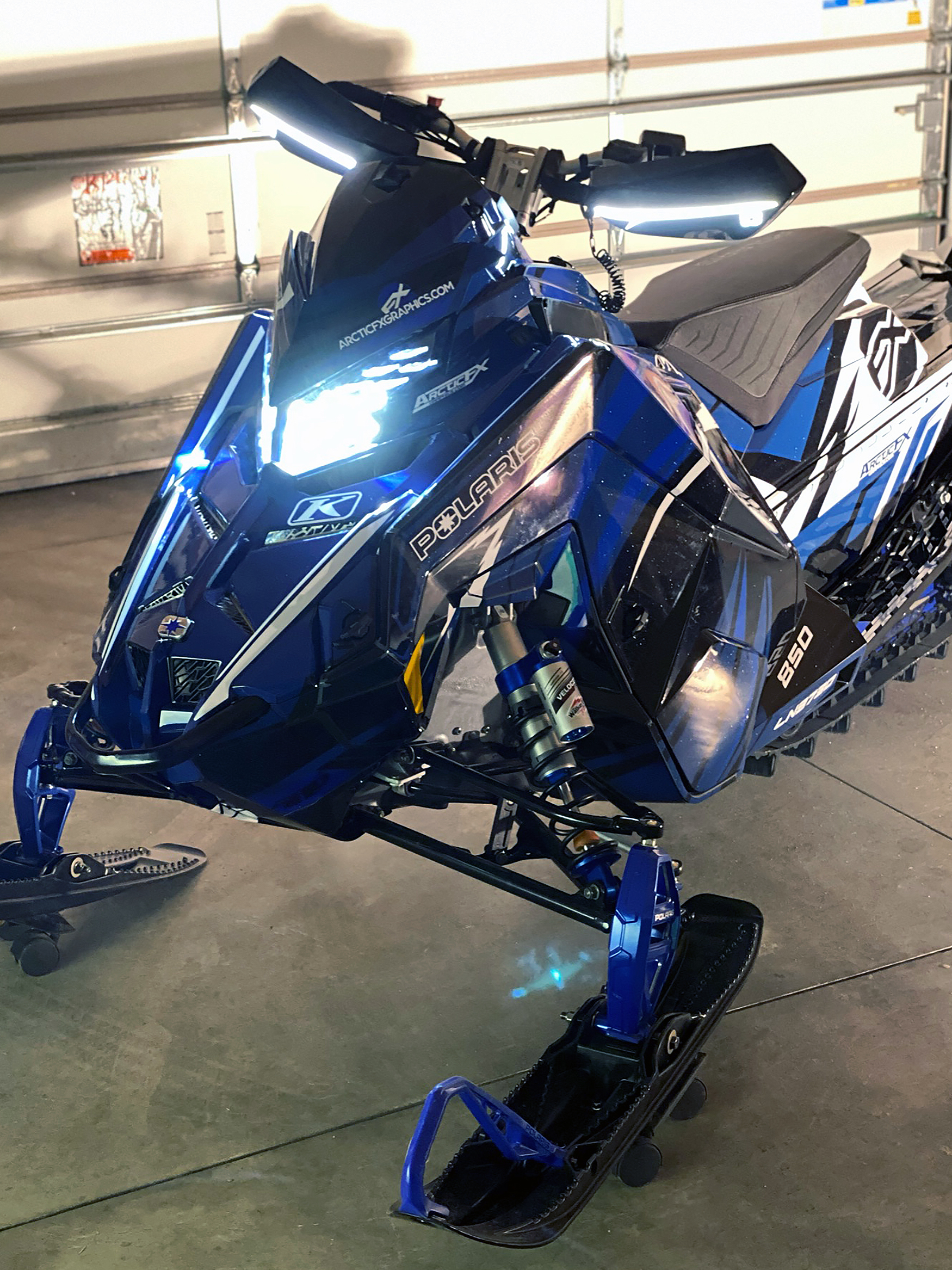 A Polaris Matryx Trail snowmobile with a white, blue, and black Kesterke Adrenaline custom vinyl wrap.