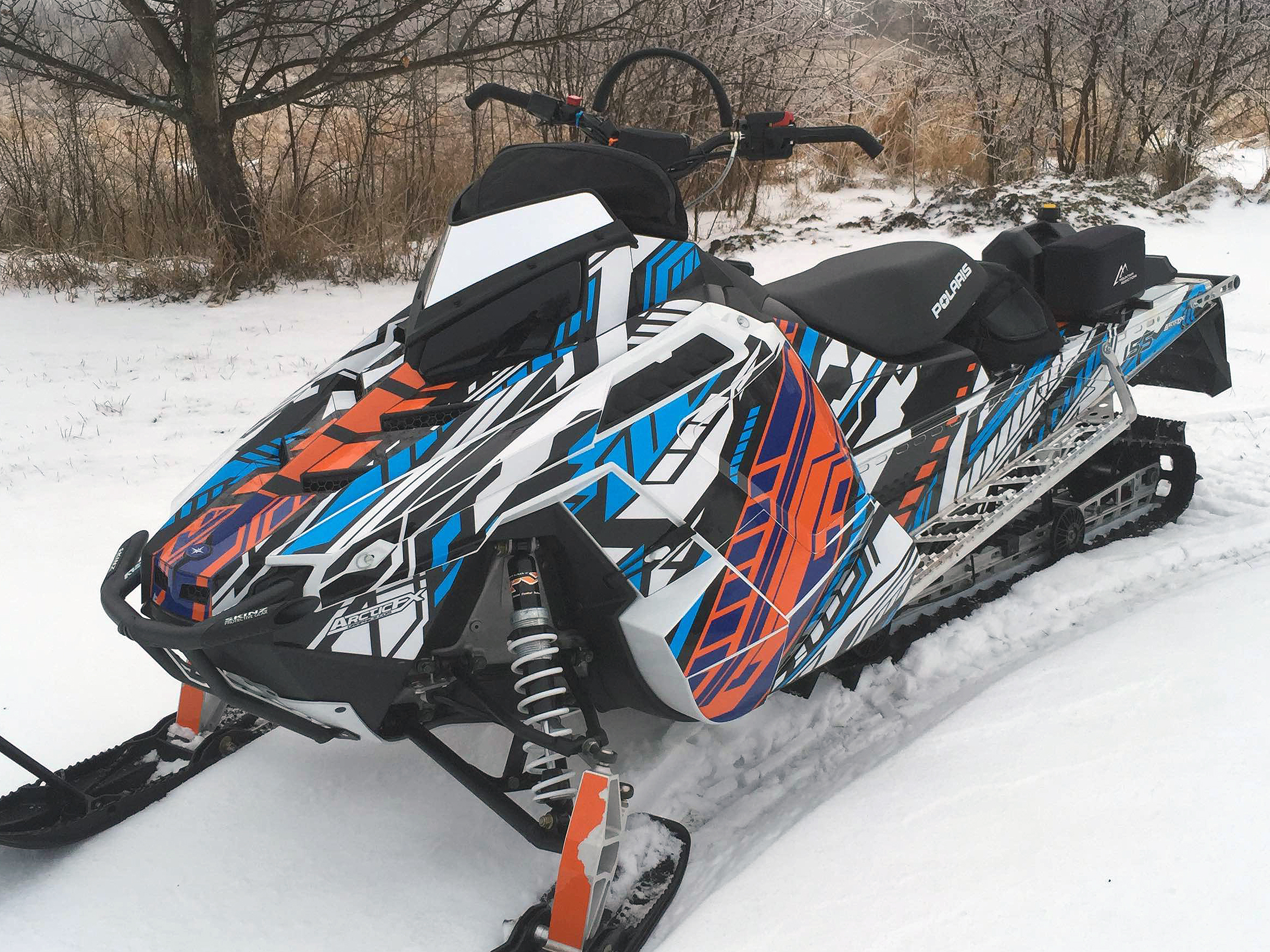 A Polaris Pro-Ride snowmobile with a orange, white, and black Evasion custom vinyl wrap.