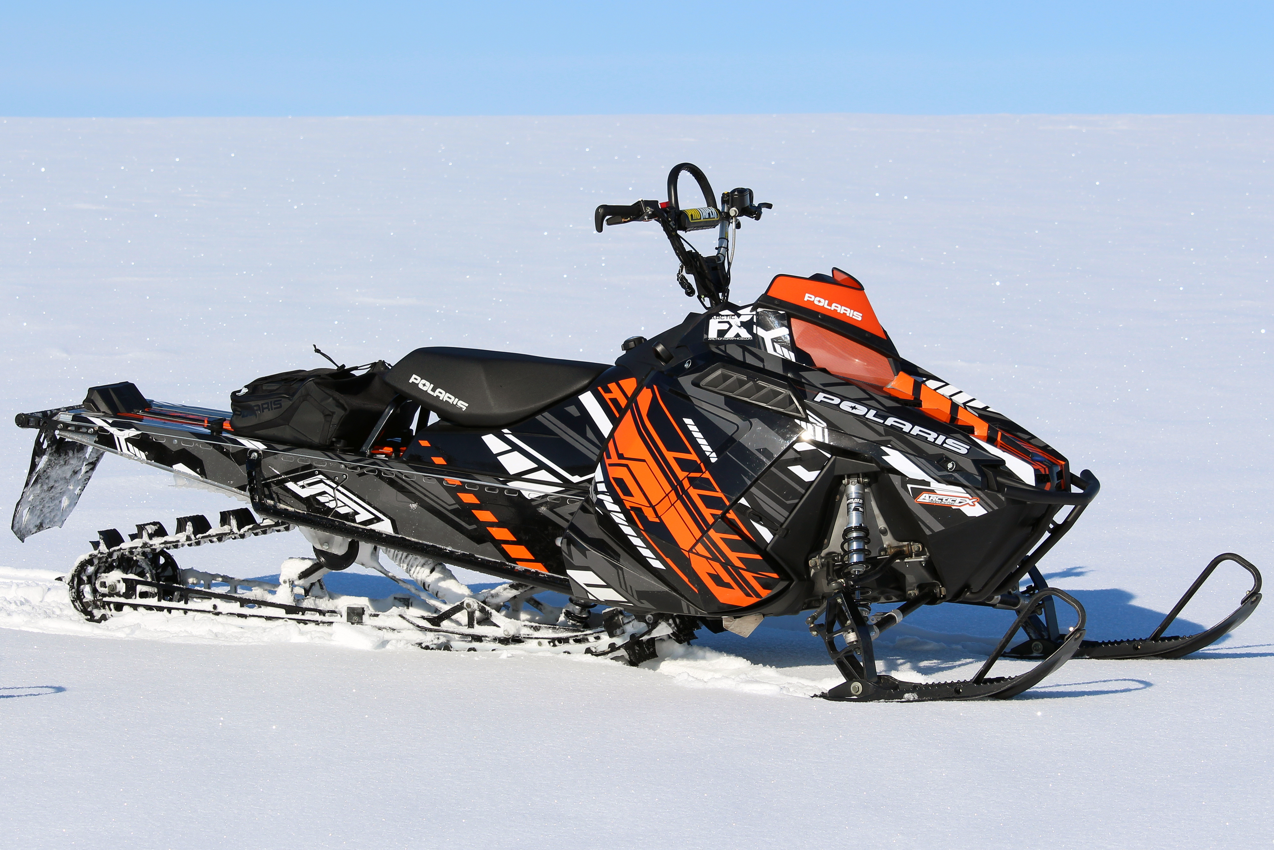 A Polaris Pro-Ride snowmobile with a orange, white, and black Evasion custom vinyl wrap.