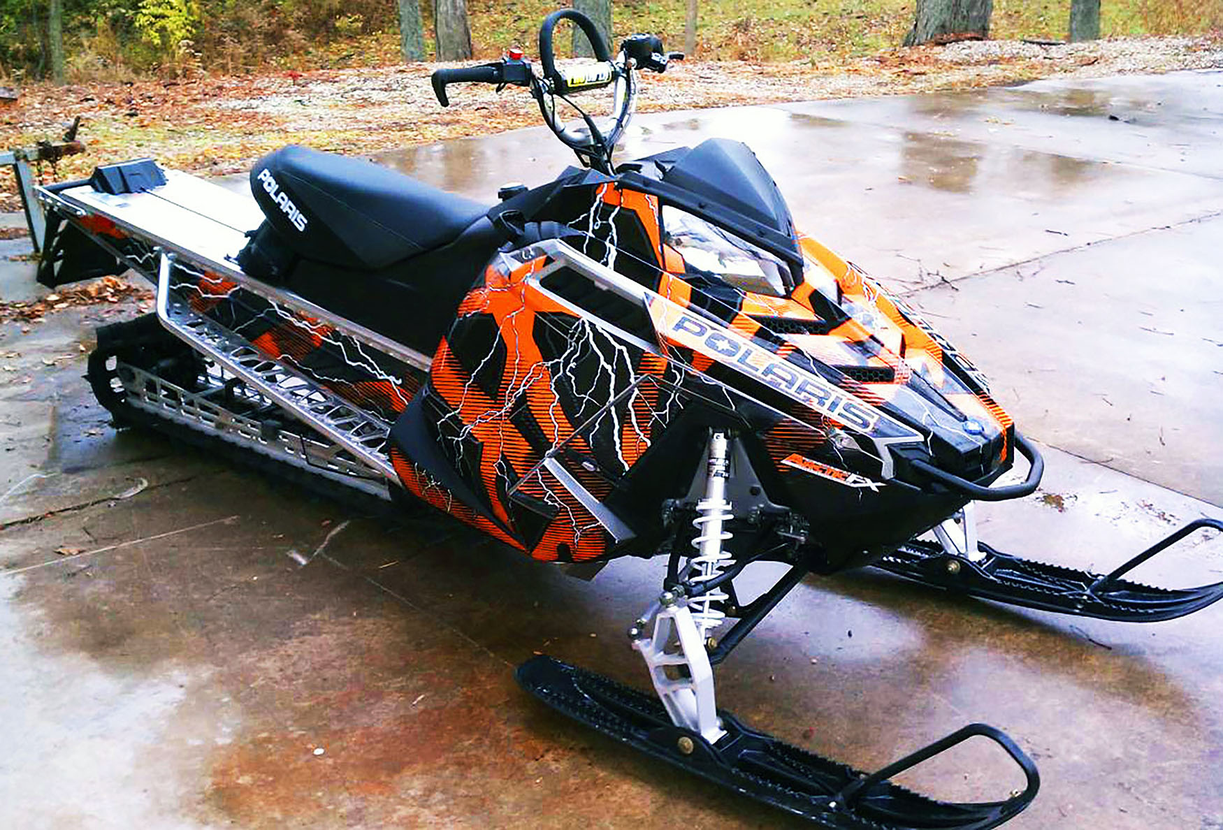 A Polaris Pro-Ride snowmobile with a orange, white, and black Hard Rain custom vinyl wrap.