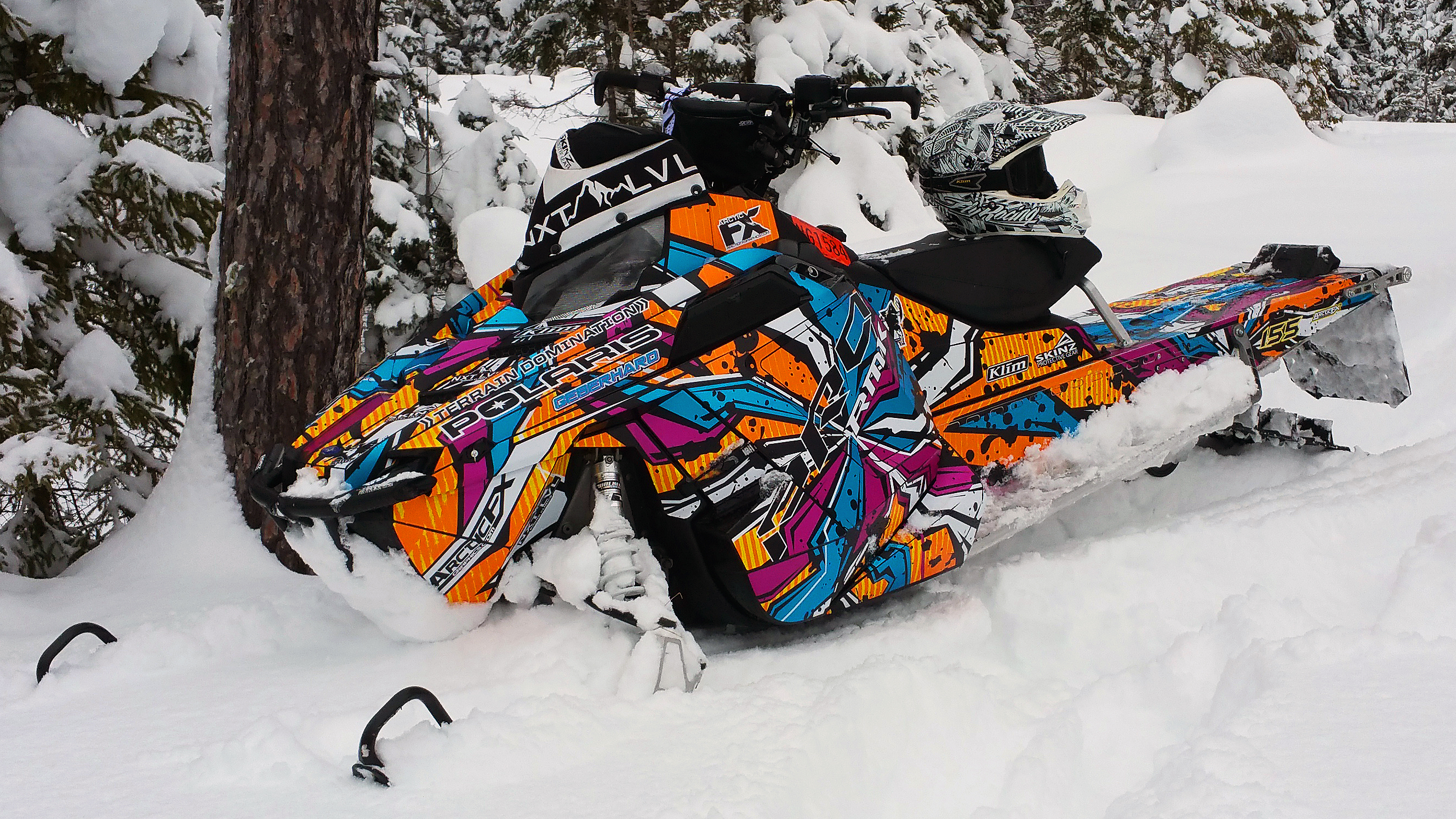 A Polaris Pro-Ride snowmobile with a orange, blue, pink, and black Stricken custom vinyl wrap.