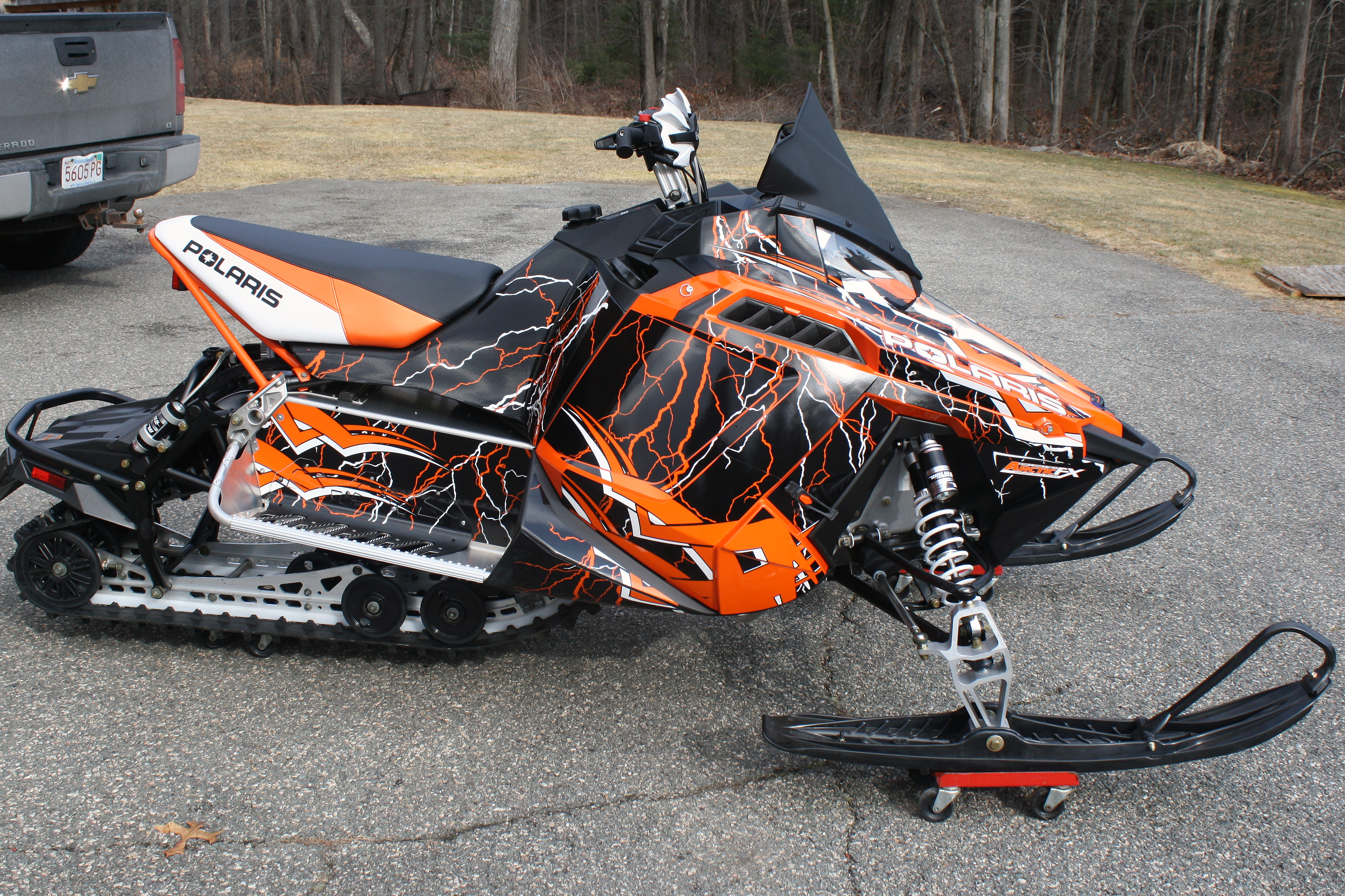A Polaris Pro-Ride snowmobile with a orange, white, and black Shock Treatment custom vinyl wrap.