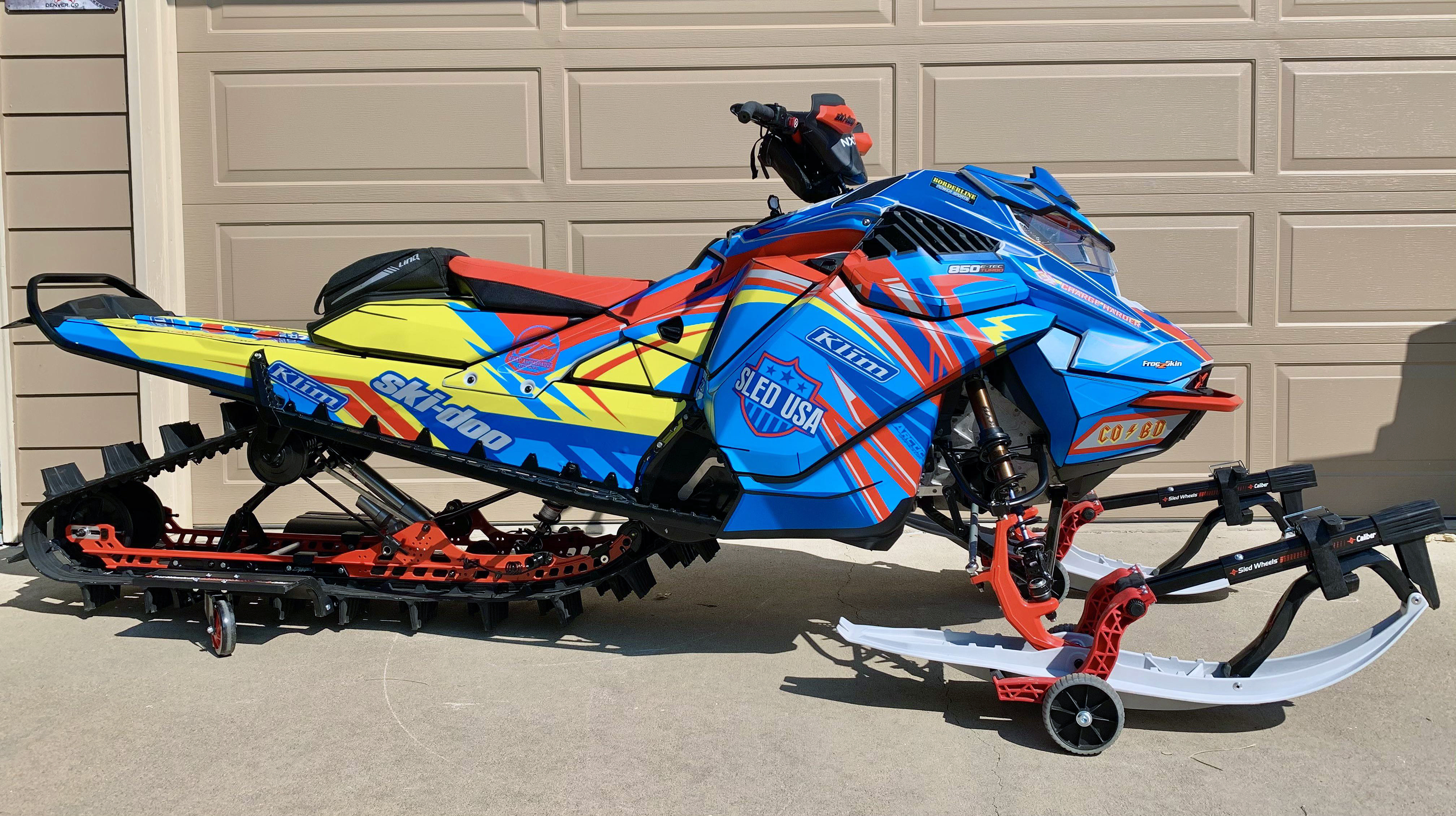 A Ski-Doo Gen4 Lightweight snowmobile with a yellow, blue, and red Kesterke Adrenaline custom vinyl wrap.