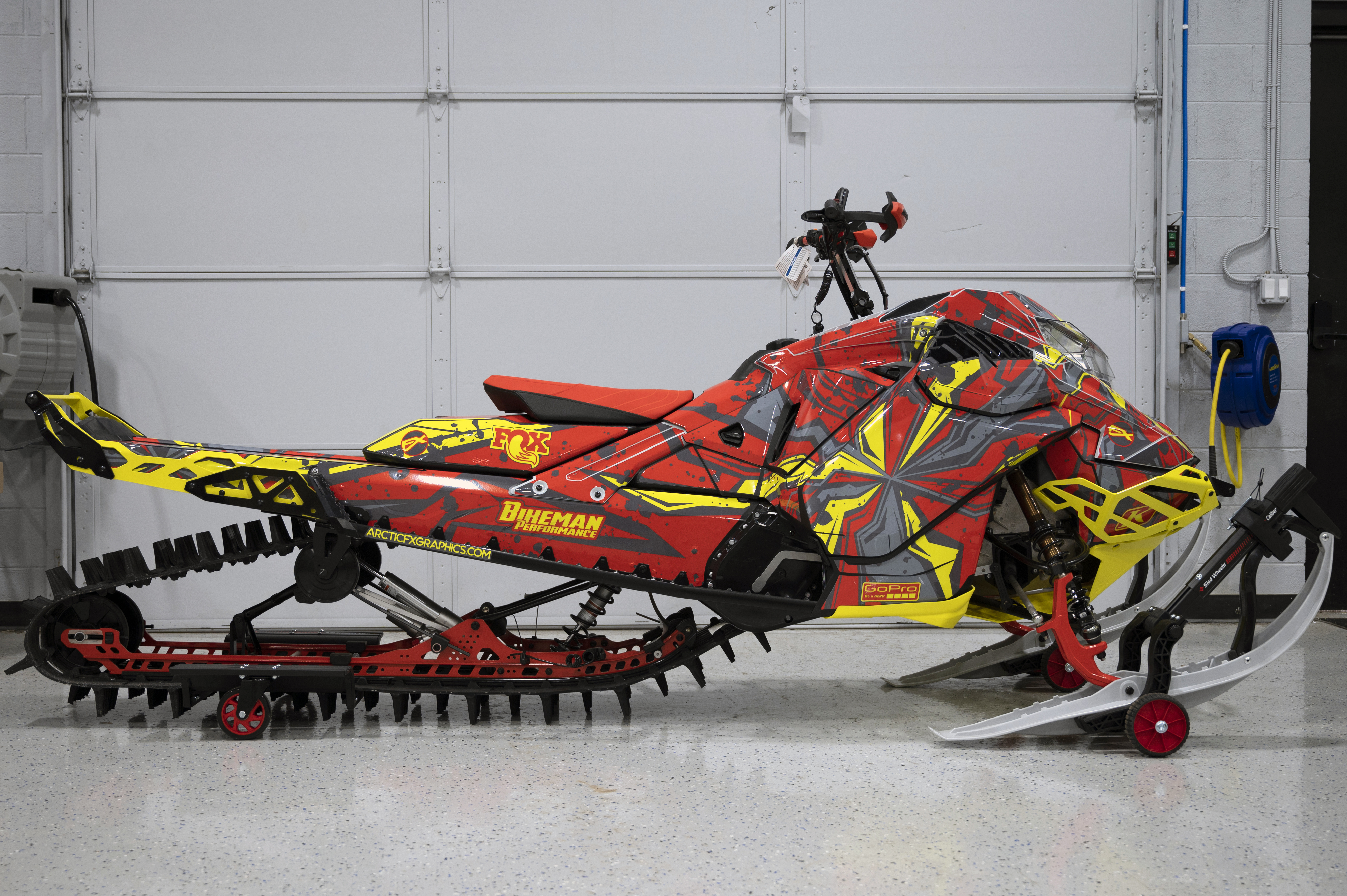 A Ski-Doo Gen4 Lightweight snowmobile with a yellow, red, and gray Stricken custom vinyl wrap.