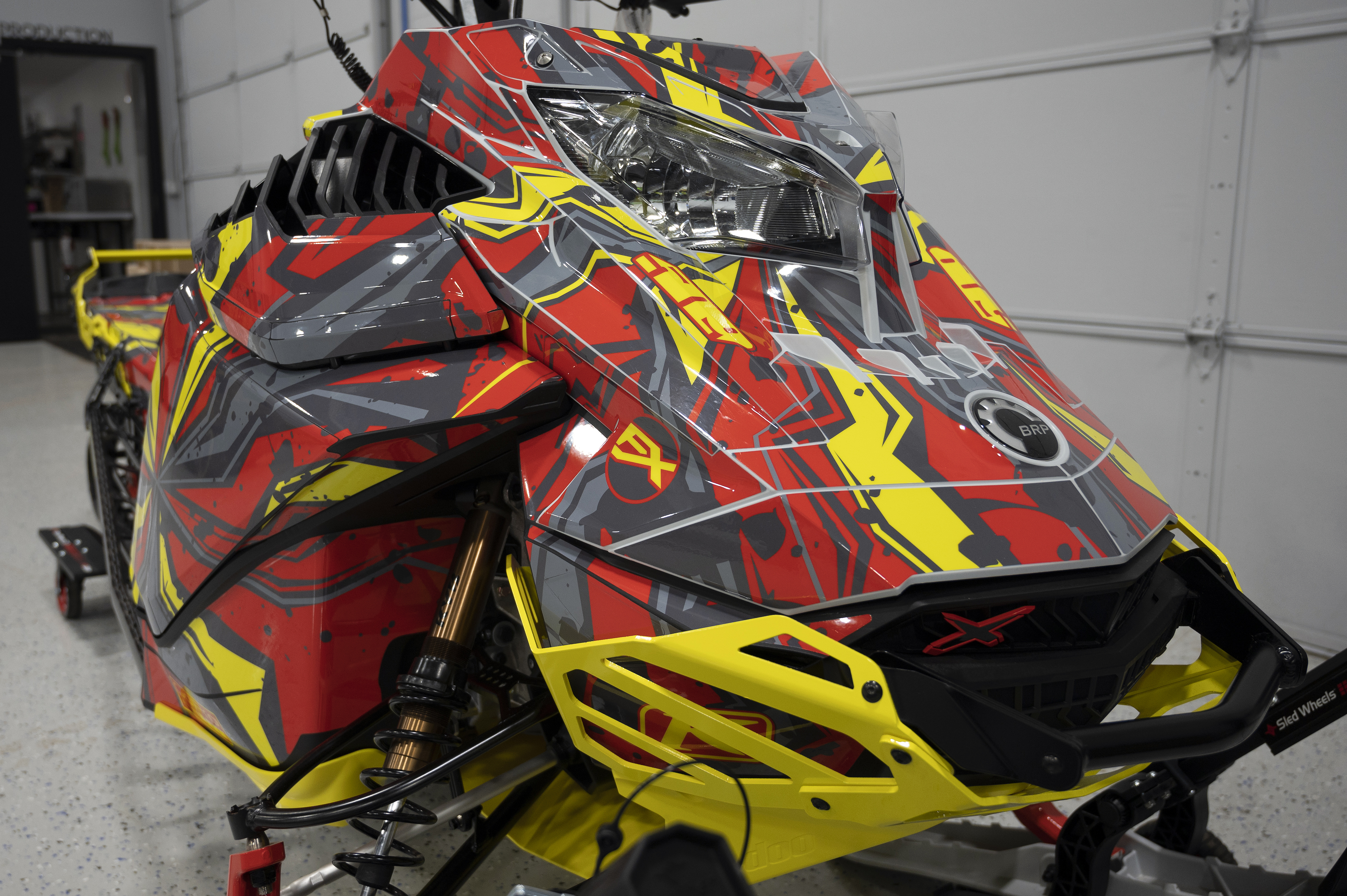 A Ski-Doo Gen4 Lightweight snowmobile with a yellow, red, and gray Stricken custom vinyl wrap.